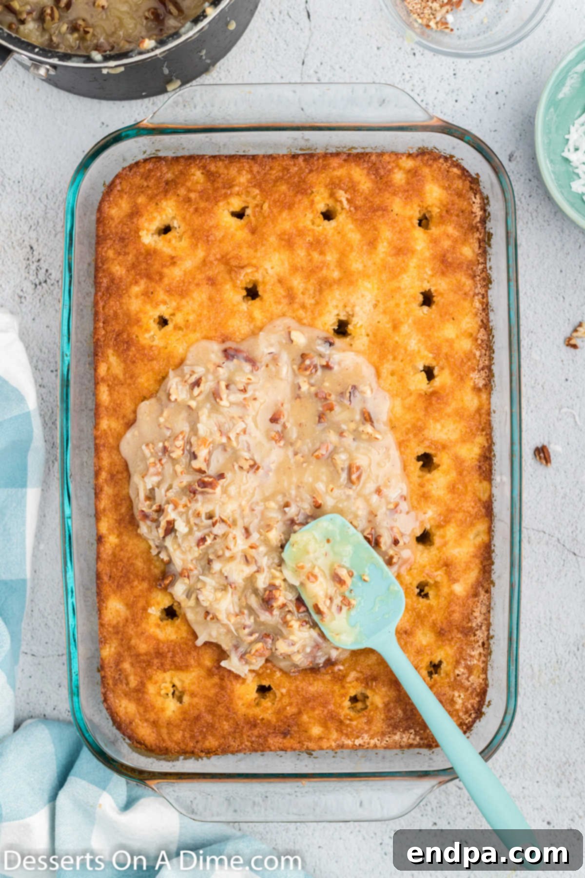 Hot coconut and pecan topping being spread over the poked cake, allowing it to soak into the holes.