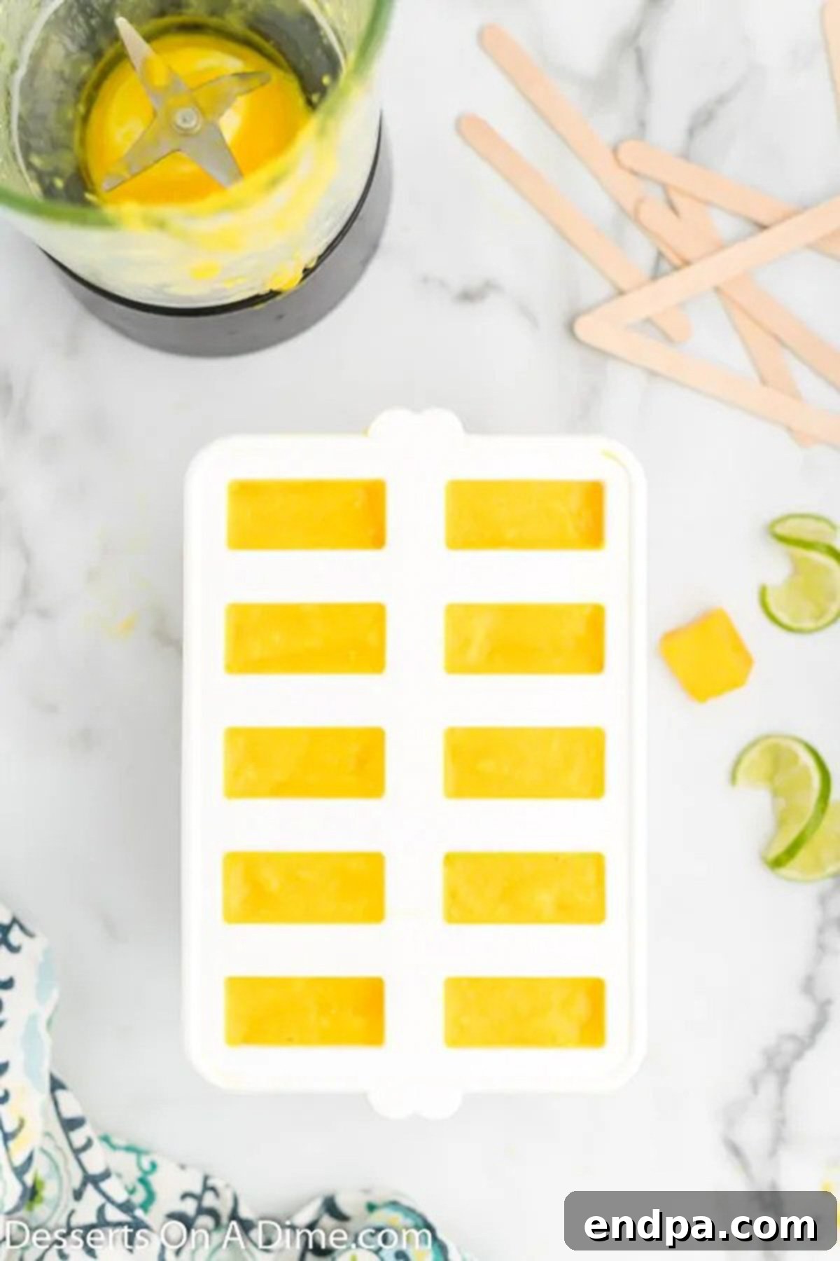 A hand pouring the vibrant mango mixture from a blender into multiple popsicle molds arranged on a tray, filling each compartment evenly.