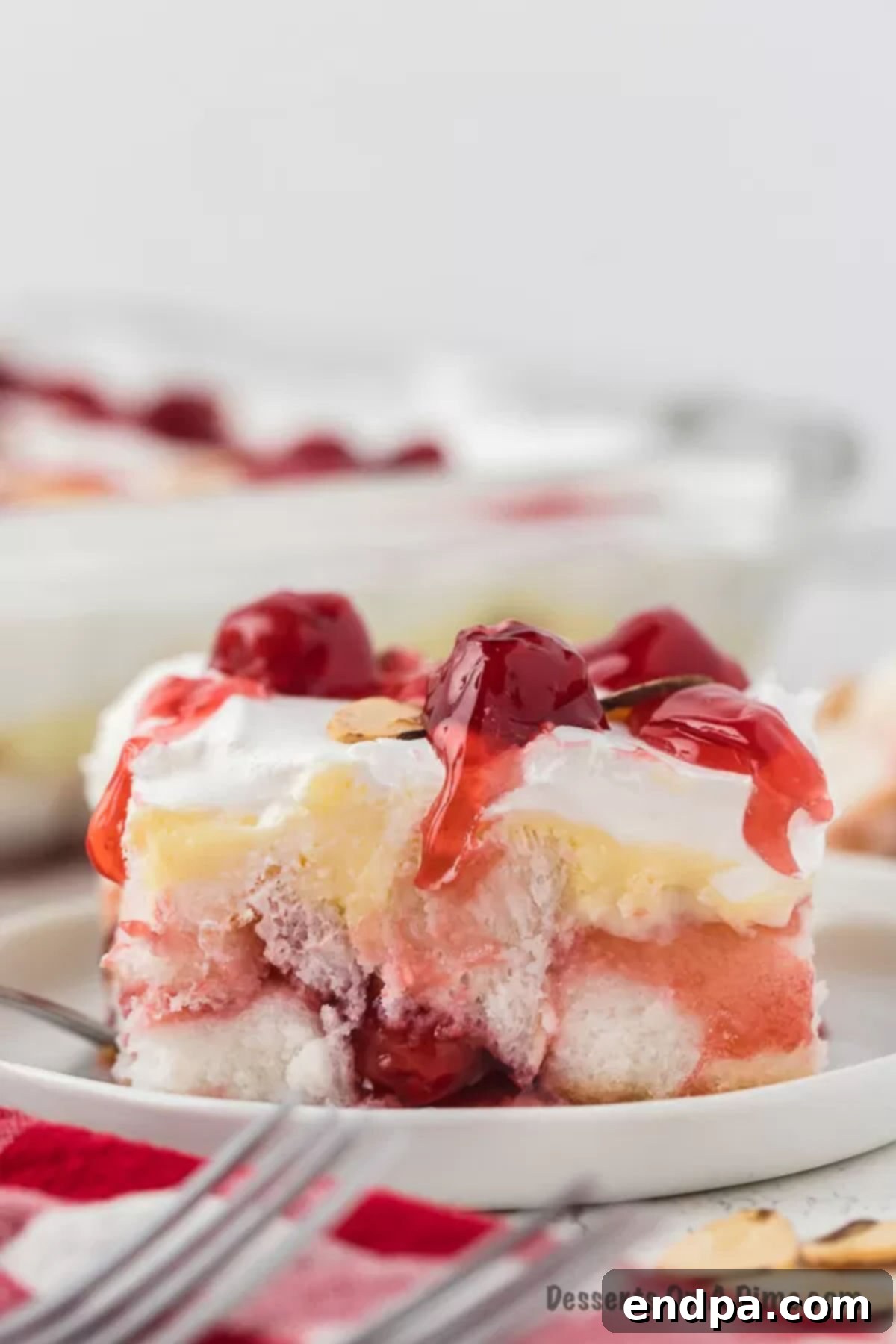 A stunning slice of Heaven on Earth Cake on a serving plate, showcasing its beautiful layers of angel food cake, creamy pudding, vibrant cherry pie filling, and fluffy whipped topping, ready to be enjoyed.