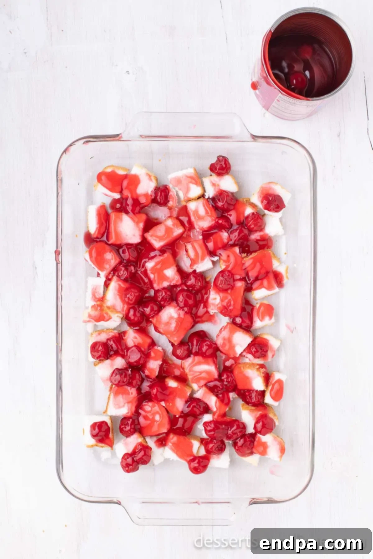 The first layer of angel food cake cubes topped with a spread of cherry pie filling in a 9x13 baking pan.
