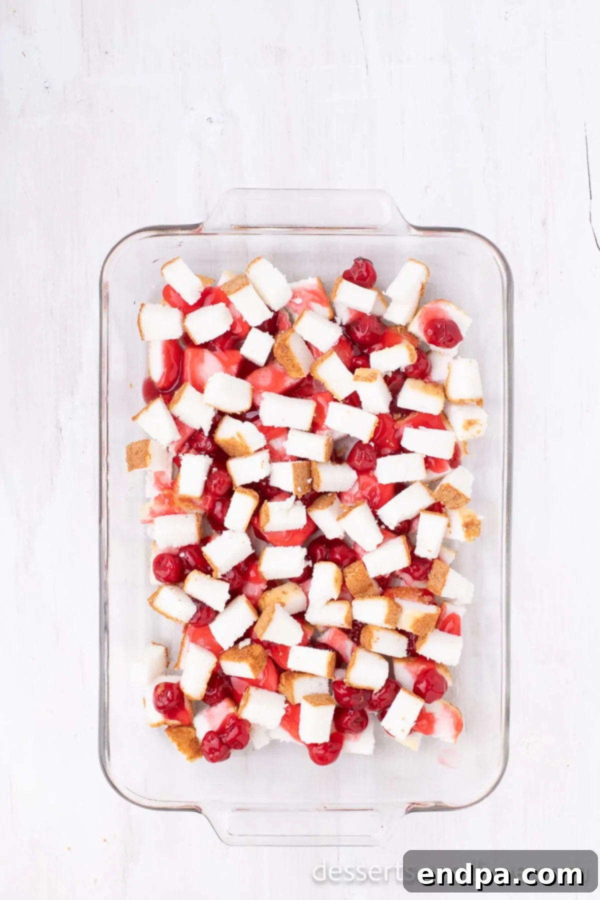 The remaining angel food cake cubes layered over the cherry pie filling in the baking dish.