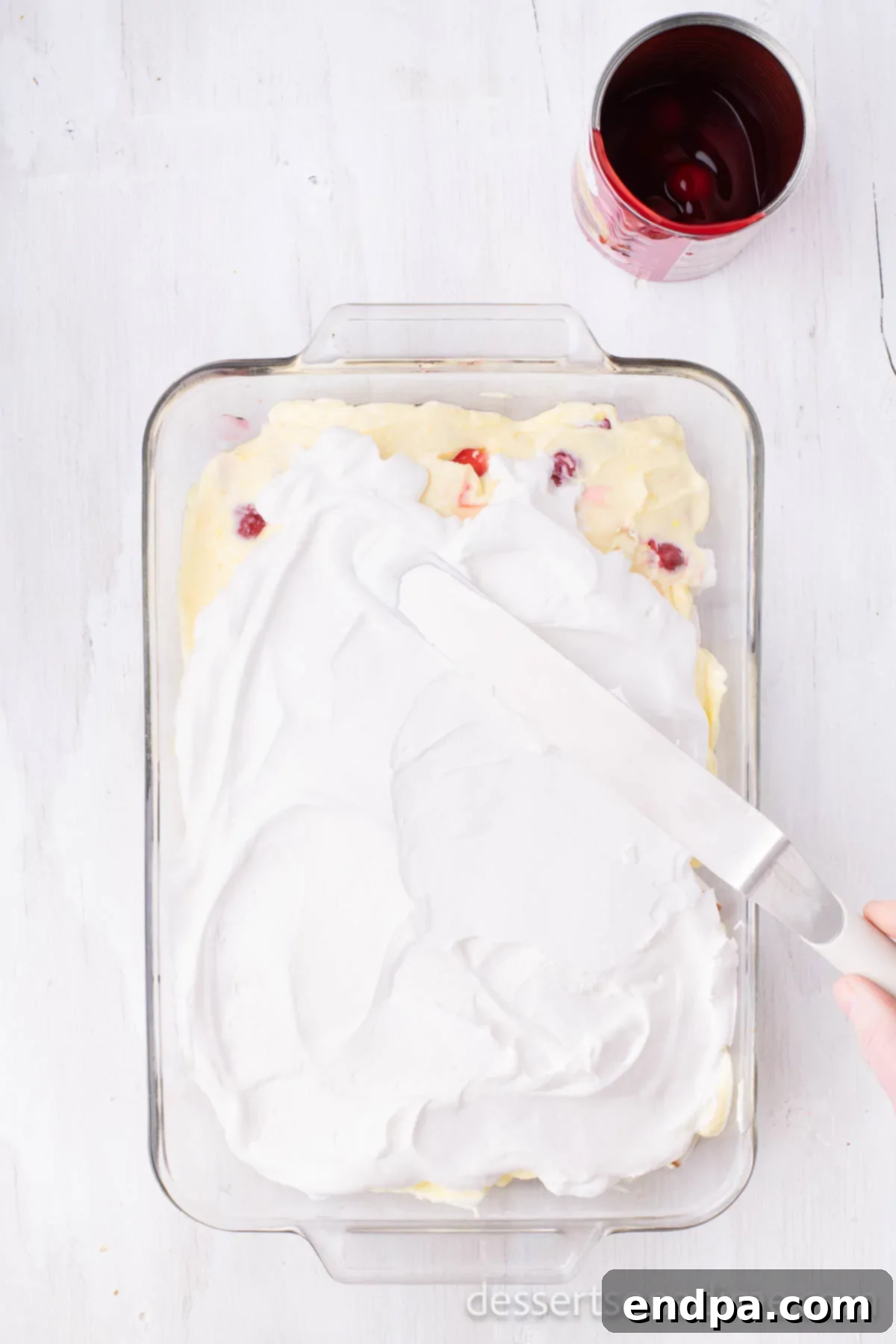 A smooth, even layer of whipped topping spread over the vanilla pudding layer, preparing the cake for its final touch.