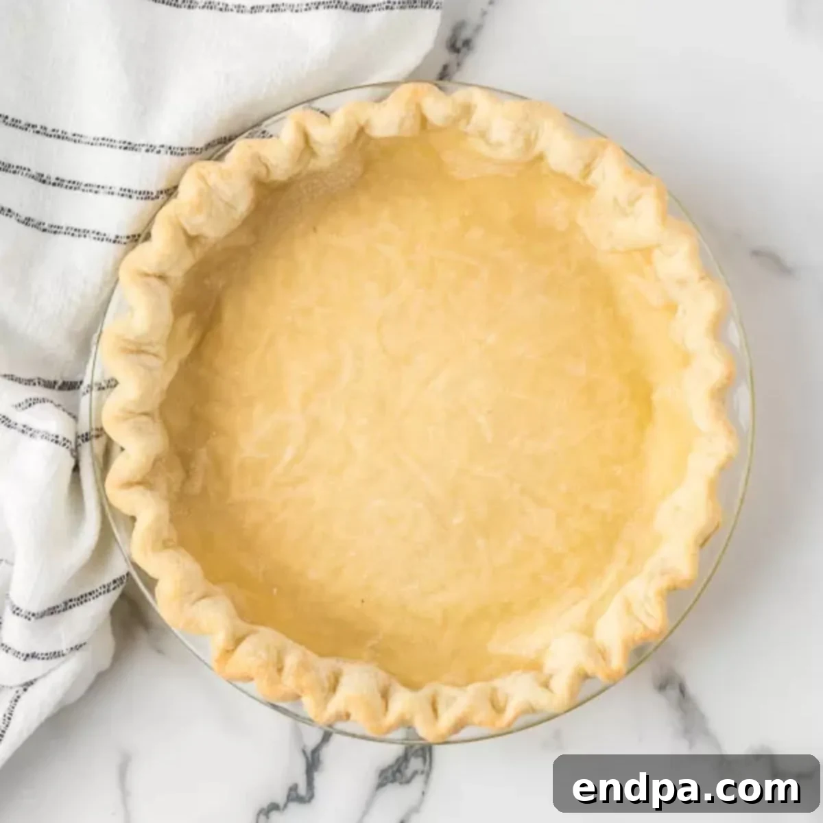 A close-up of a rustic, golden-baked pie crust resting on a marble counter, poised for a delicious filling.