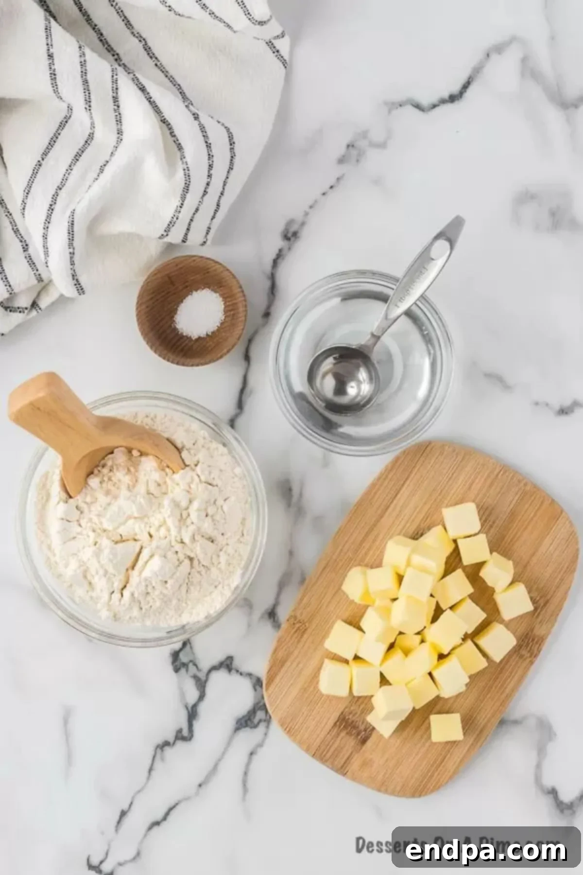 Three core ingredients for making a pie crust: perfectly cubed cold butter, a bowl of all-purpose flour, and a glass of ice-cold water.
