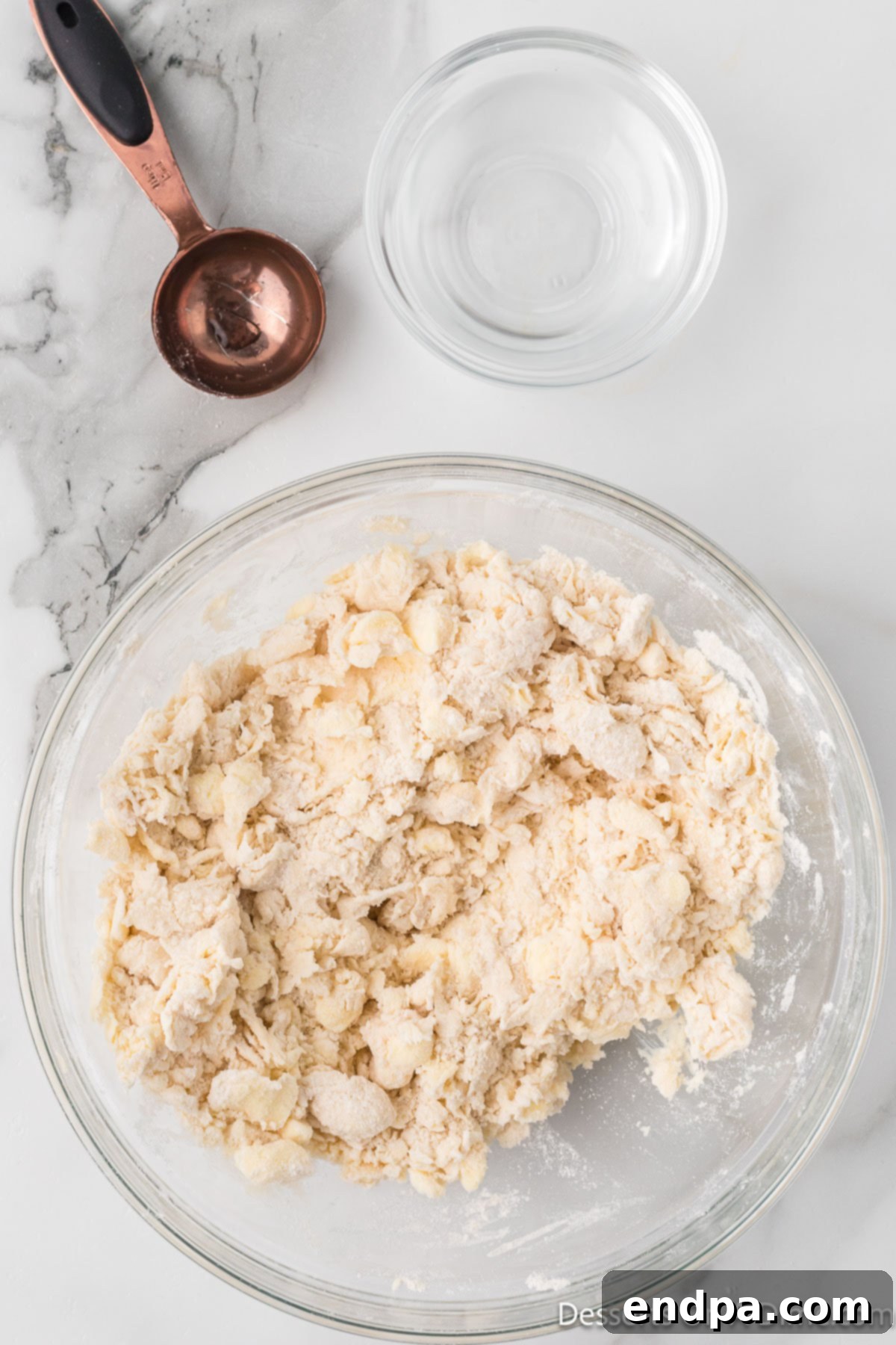 Ice-cold water being gradually introduced to the flour and butter mixture in a bowl, mixing gently.