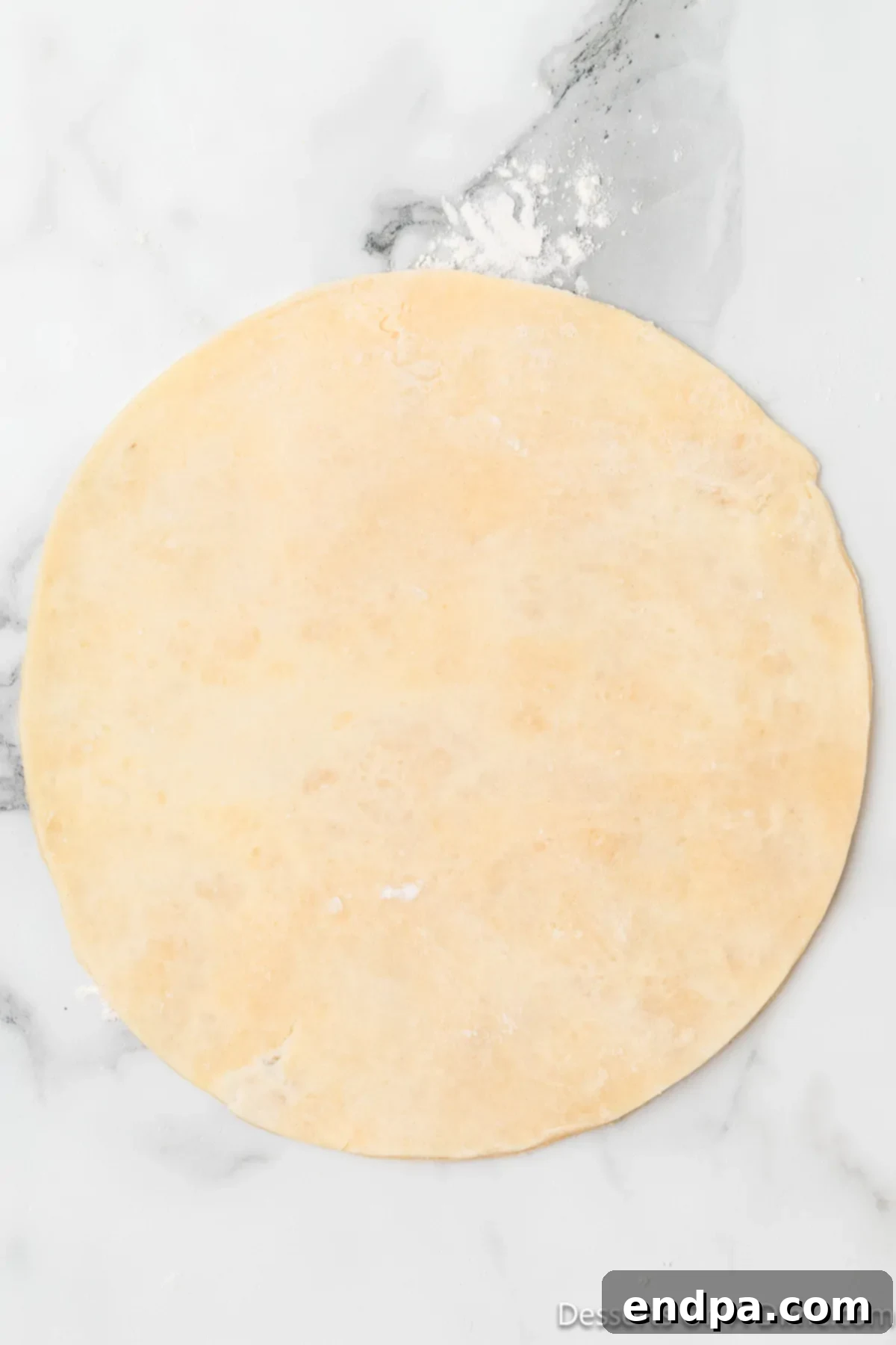 The chilled pie dough being skillfully rolled out into a perfectly circular shape on a lightly floured surface using a rolling pin.