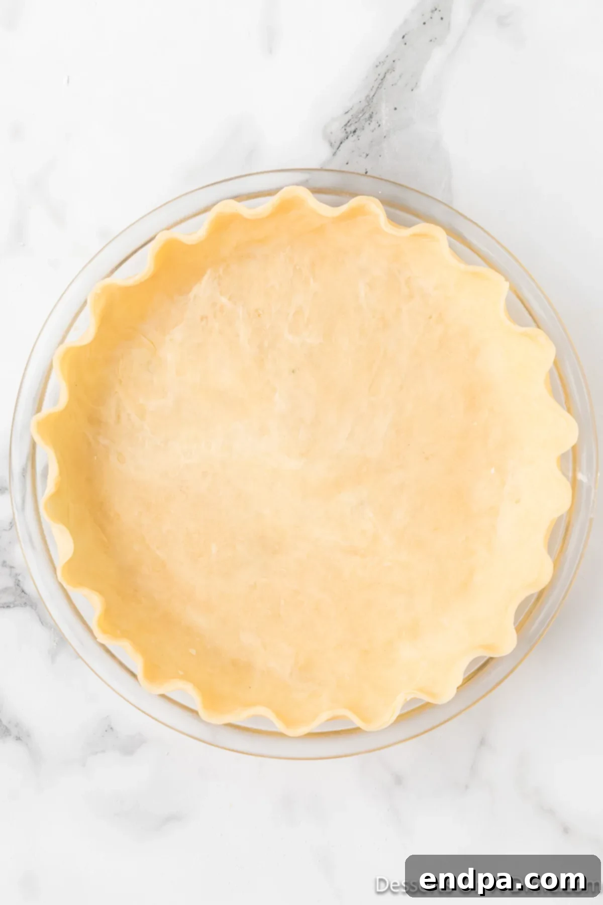 The pie crust artfully placed in the pie plate, with excess dough meticulously trimmed and the edges decoratively crimped.