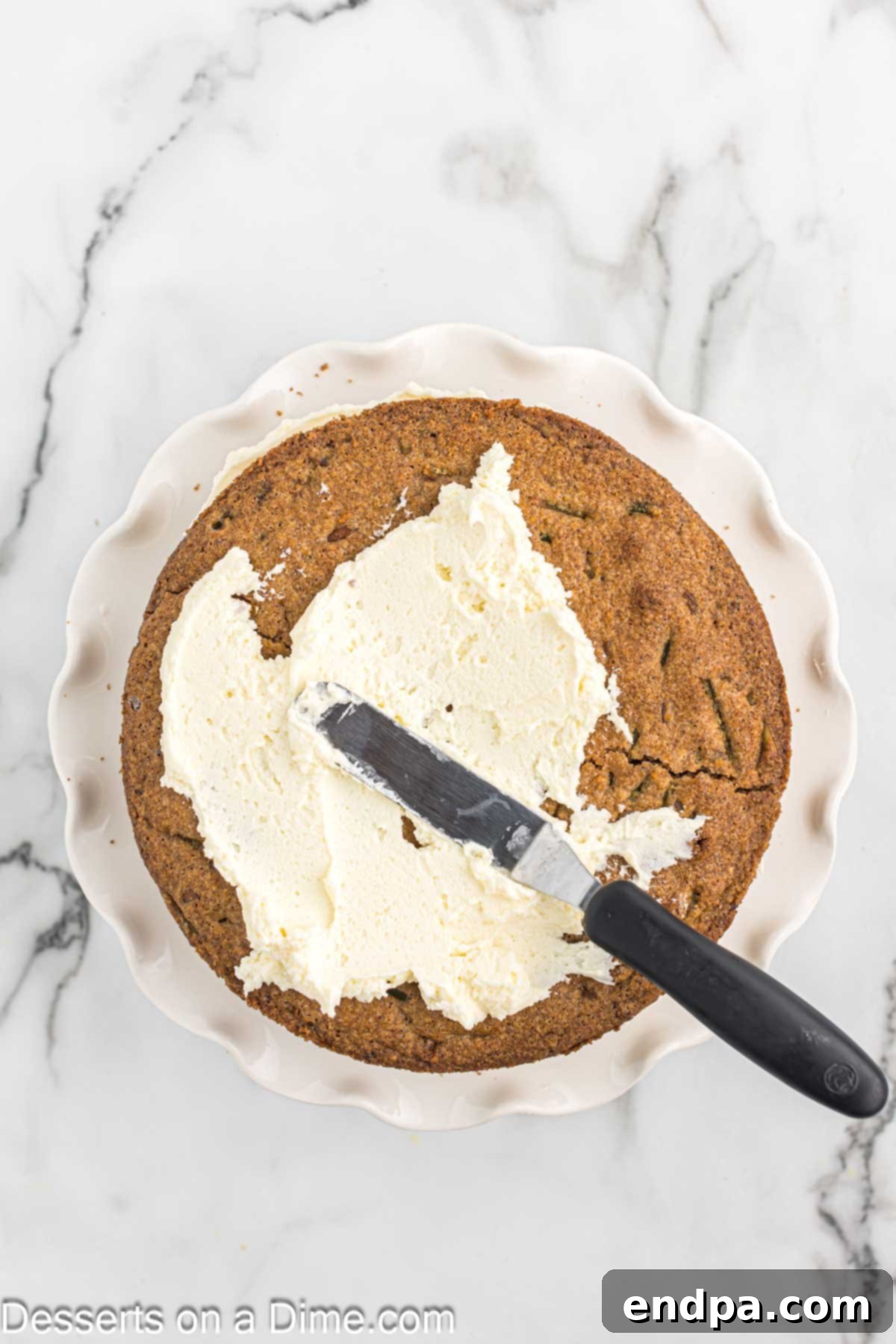 The first layer of keto carrot cake on a plate, topped with a generous amount of cream cheese frosting.