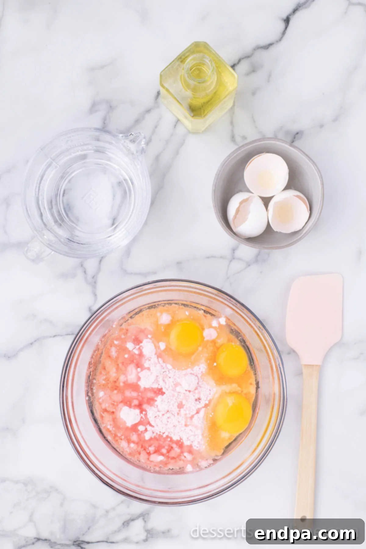 Mixing bowl with strawberry cake batter and ingredients.