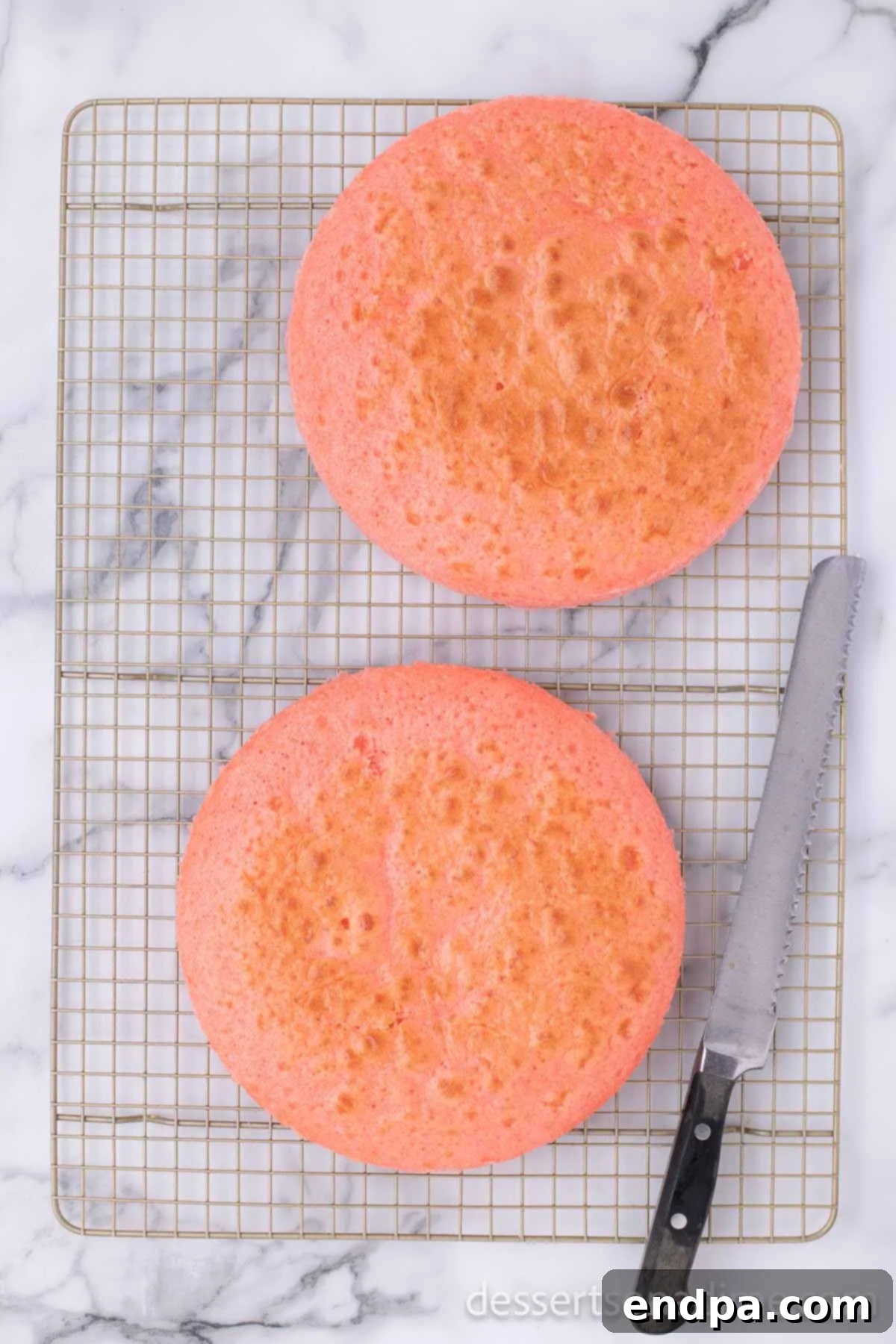 Two baked strawberry cake layers cooling on a wire rack.