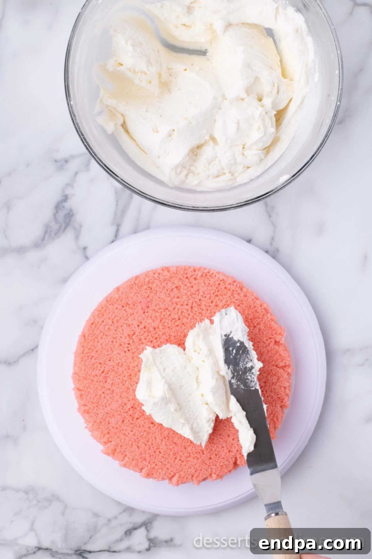 First layer of strawberry cake topped with a generous layer of buttercream frosting.