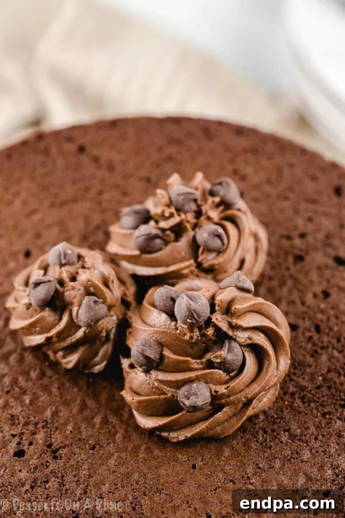 Close up image of rich, creamy keto chocolate frosting on a perfectly baked cake, garnished with a few keto-friendly chocolate shavings.