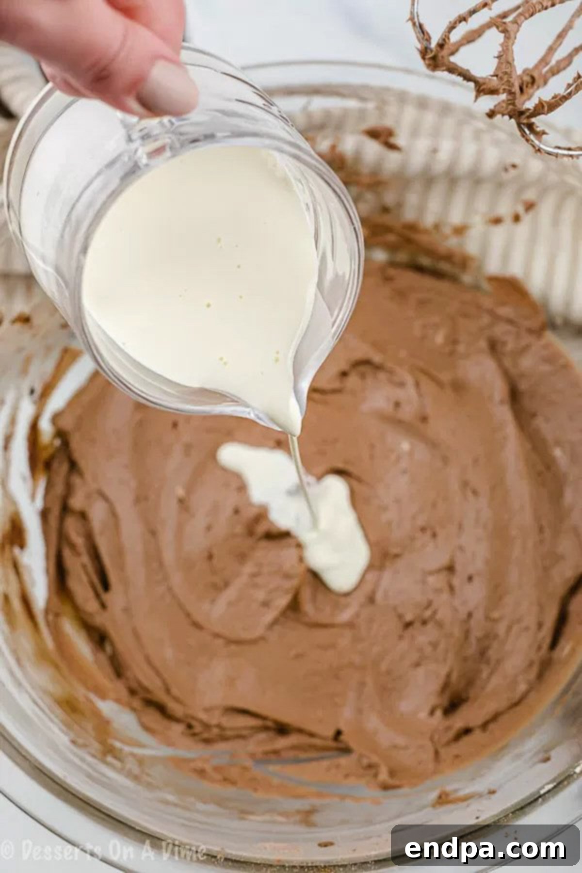 The process of gradually pouring heavy cream into the chocolate frosting mixture, as it's being whipped to achieve a spreadable consistency.