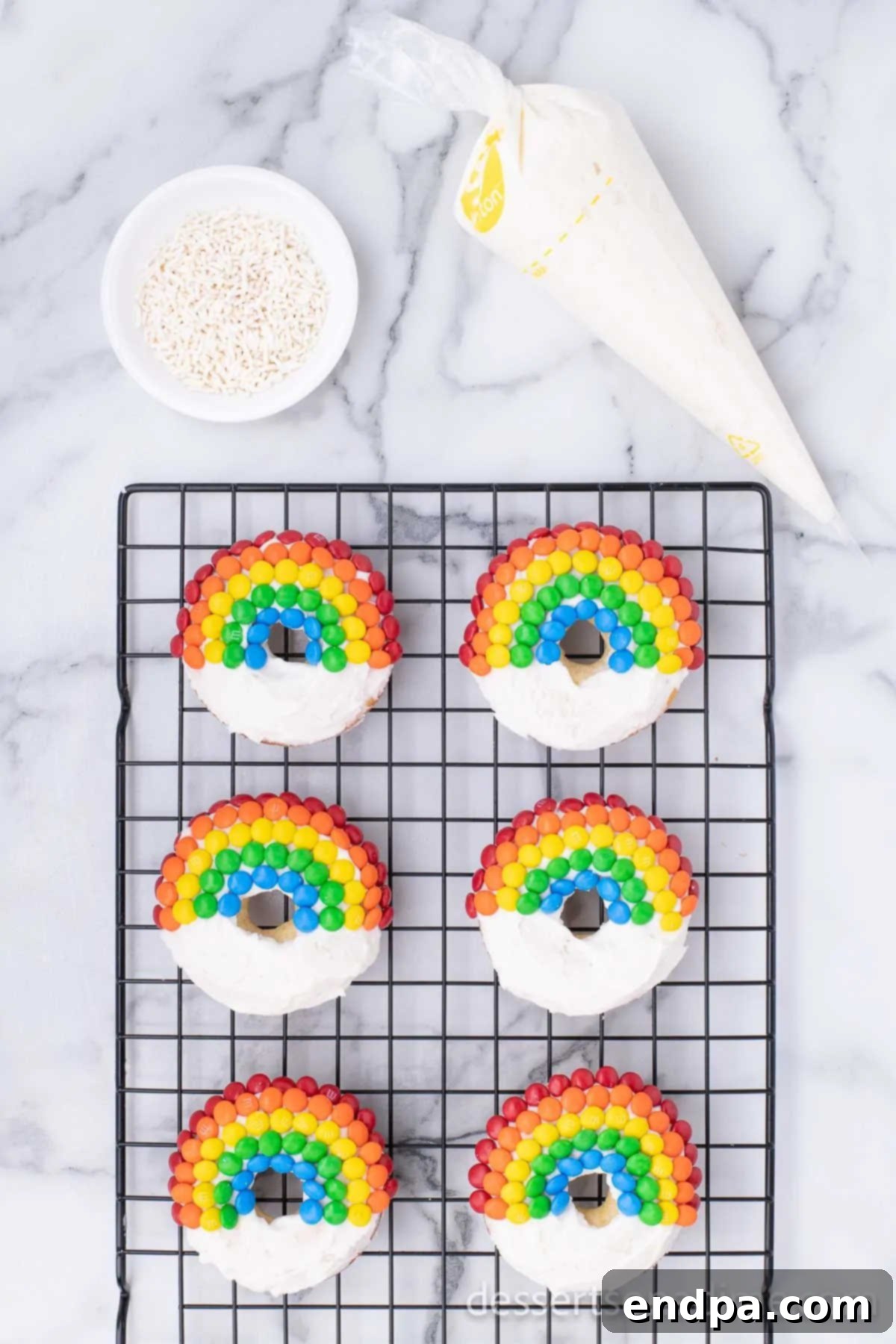 Donuts decorated with mini M&M's arranged in a rainbow arc, with white frosting clouds and sprinkles at the ends.