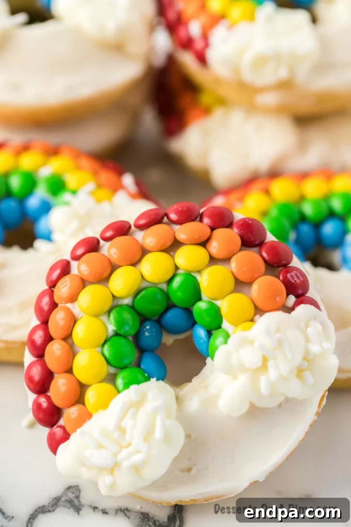 A close-up shot of a single Rainbow Donut, leaning against a stack of similar donuts, highlighting its intricate colorful design.