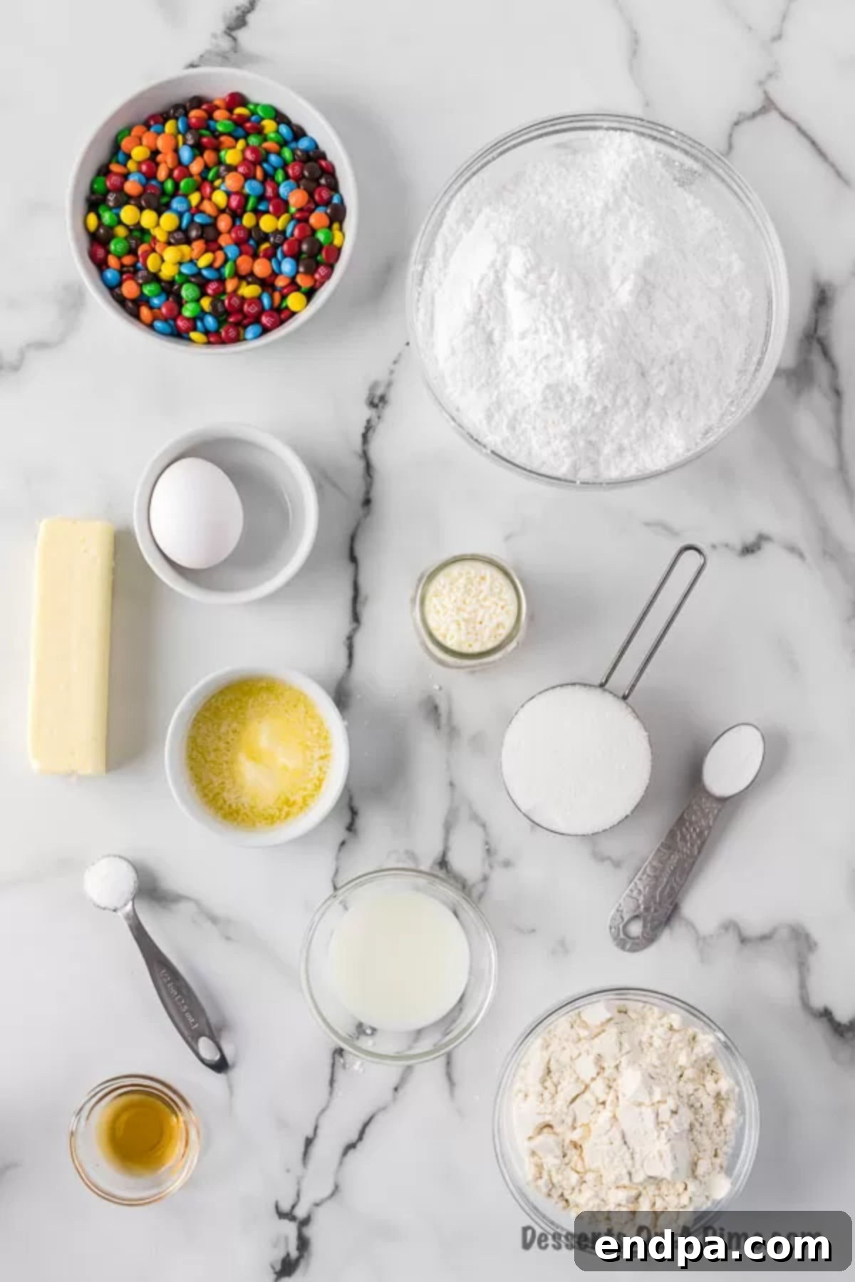 All the necessary ingredients laid out for making homemade Rainbow Donuts, including flour, sugar, baking powder, salt, butter, powdered sugar, vanilla extract, mini M&M's, and white sprinkles.