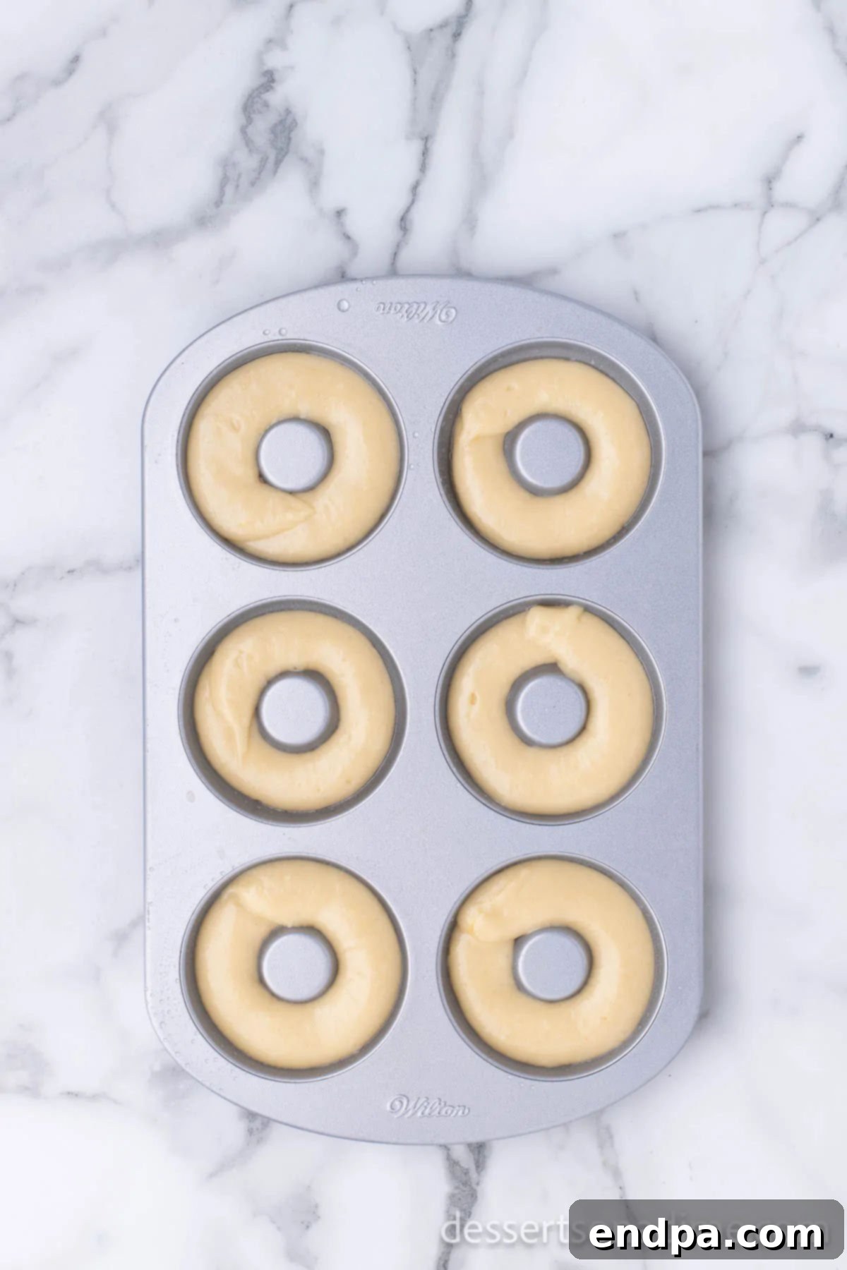 Donut batter neatly piped into the cavities of a donut baking pan, ready for the oven.