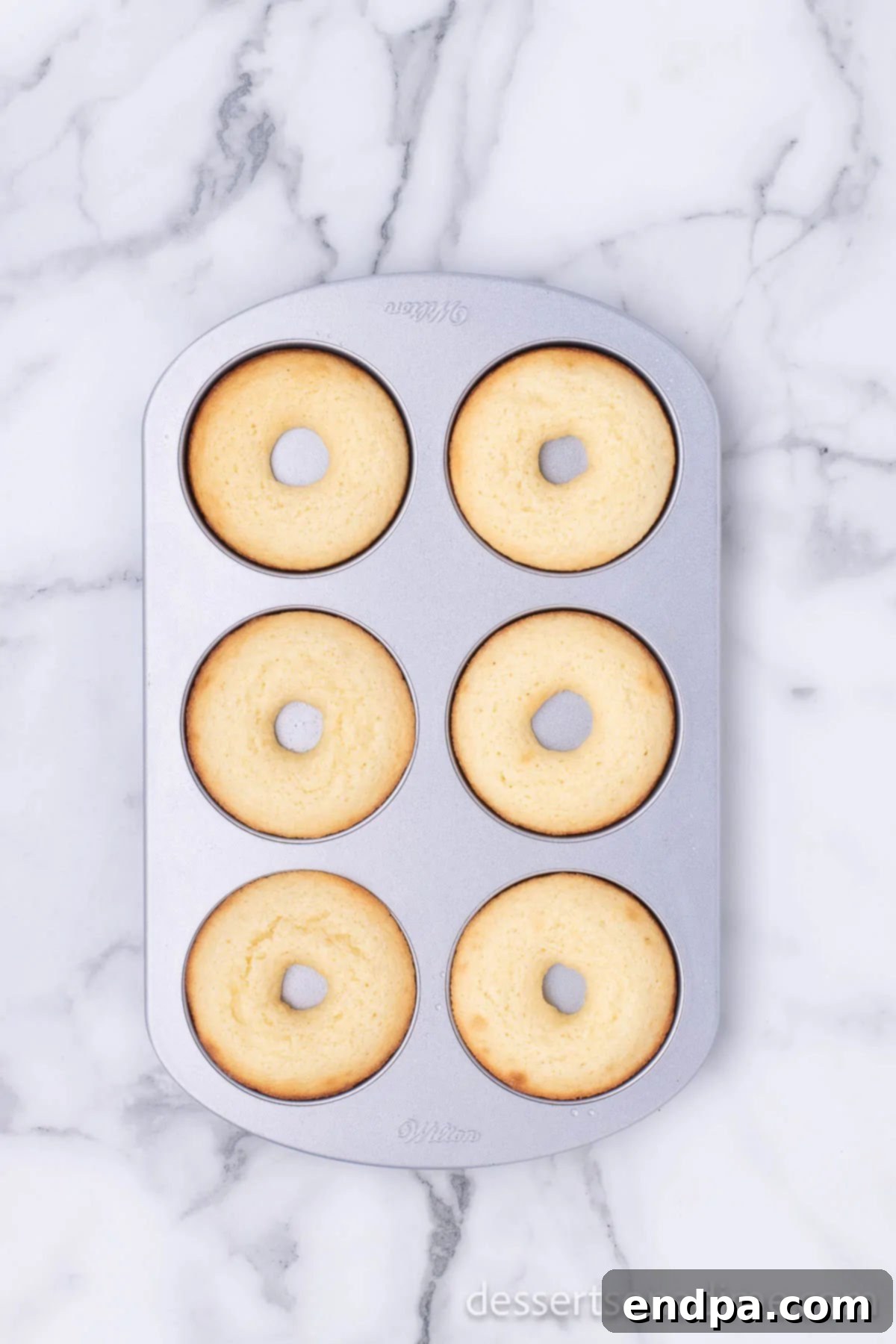 Baked donuts cooling in the donut pan, having risen perfectly golden brown.