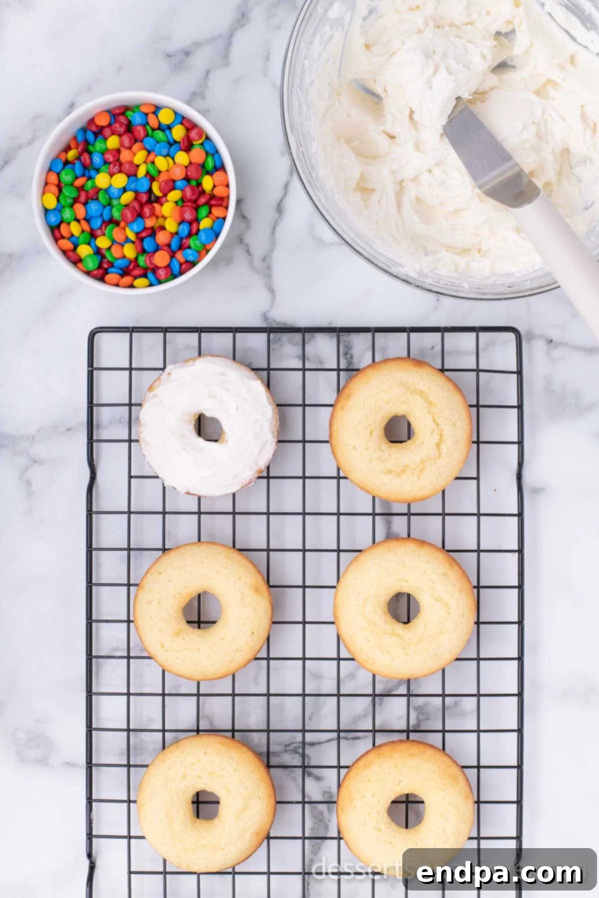 Cooled donuts with a generous layer of white frosting on a wire rack, ready for further decoration.