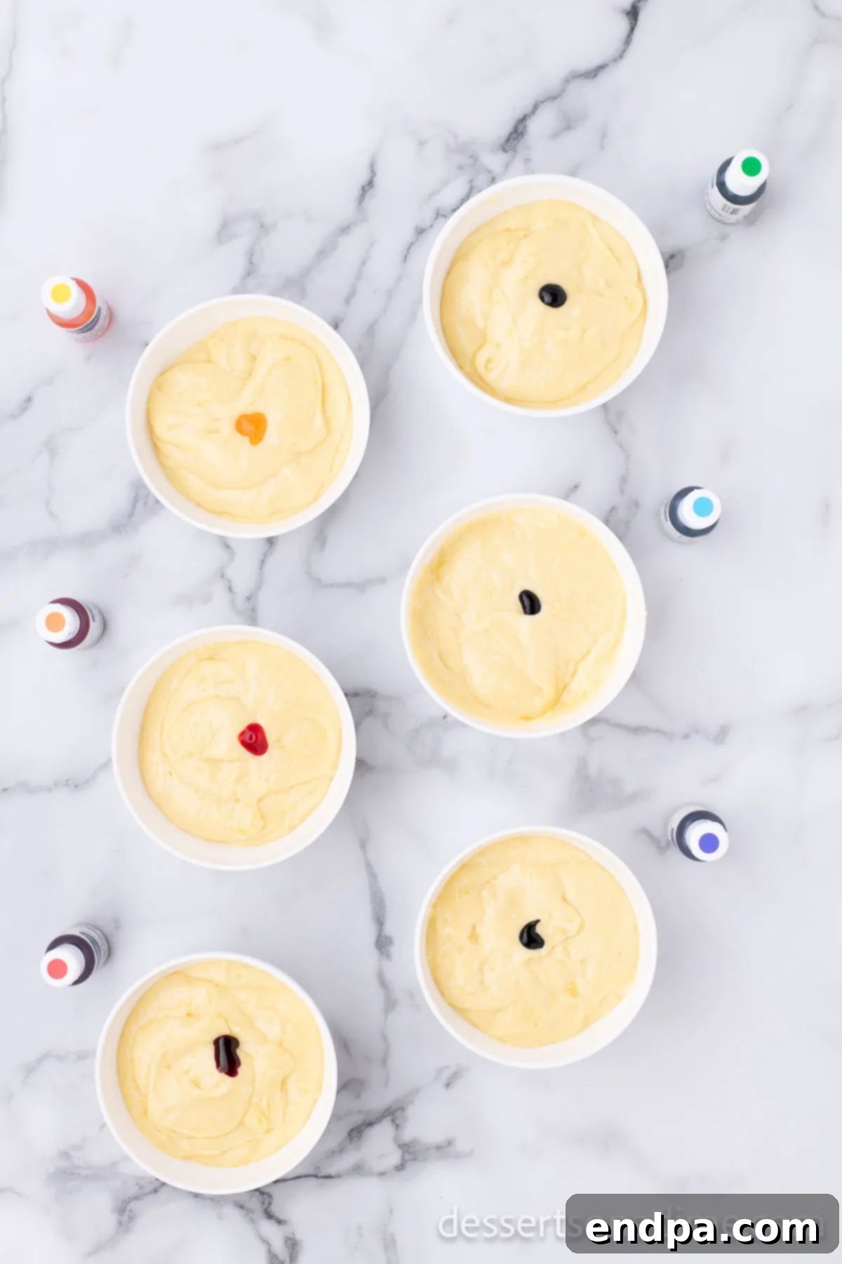 Cake batter divided into small bowls, each with a different gel food coloring.