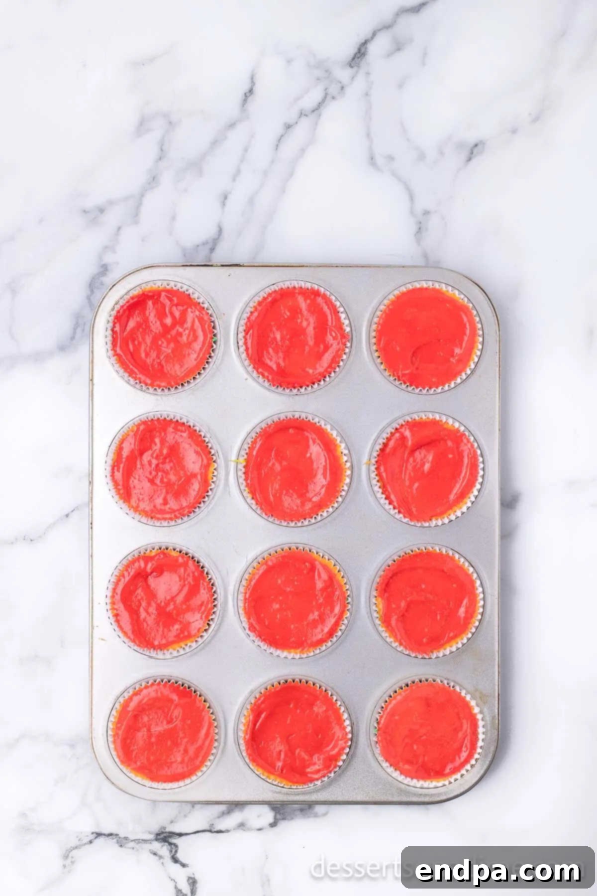 Colored batter being piped in layers into each cupcake liner.