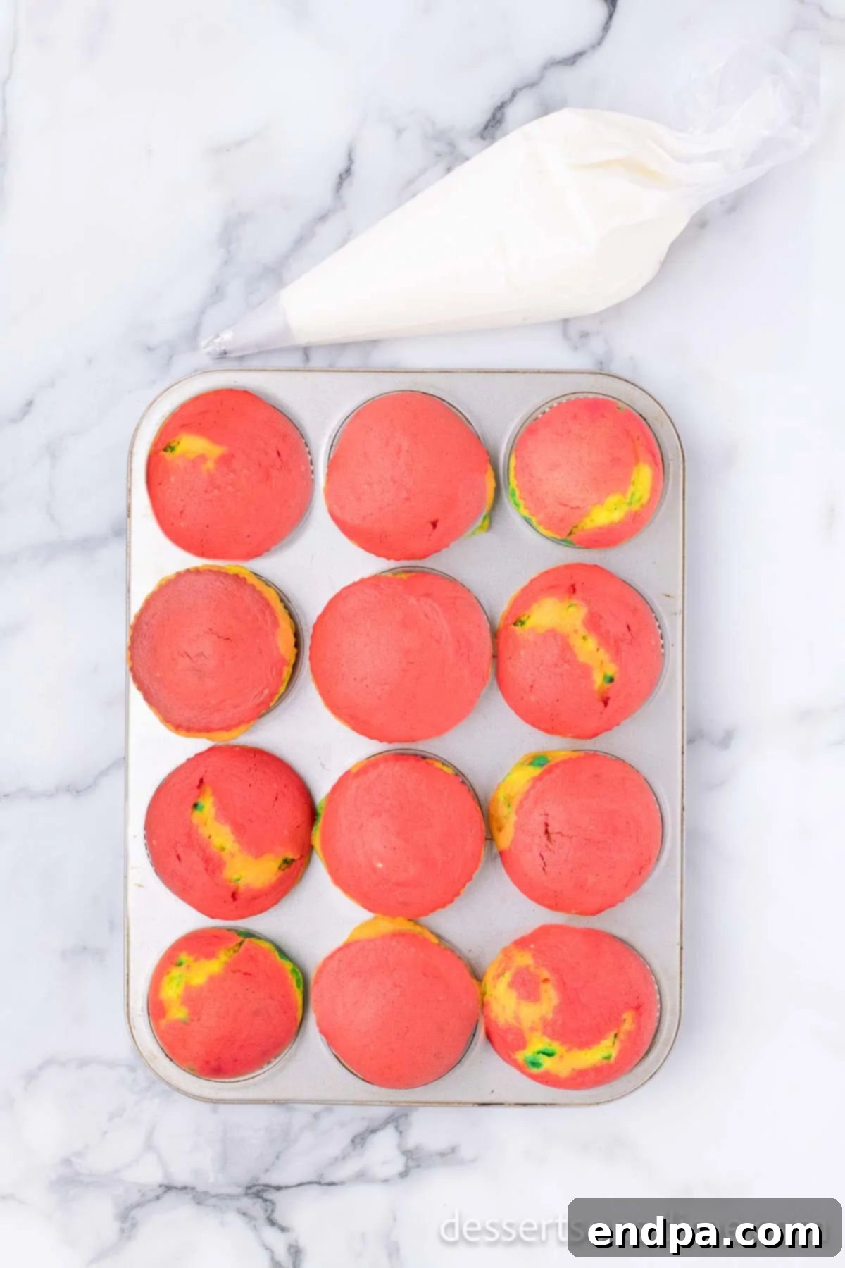 Baked rainbow cupcakes cooling on a wire rack.