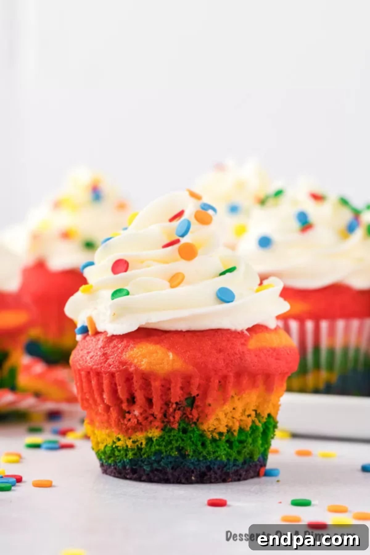 Beautiful rainbow cupcakes with fluffy white icing and colorful sprinkles.