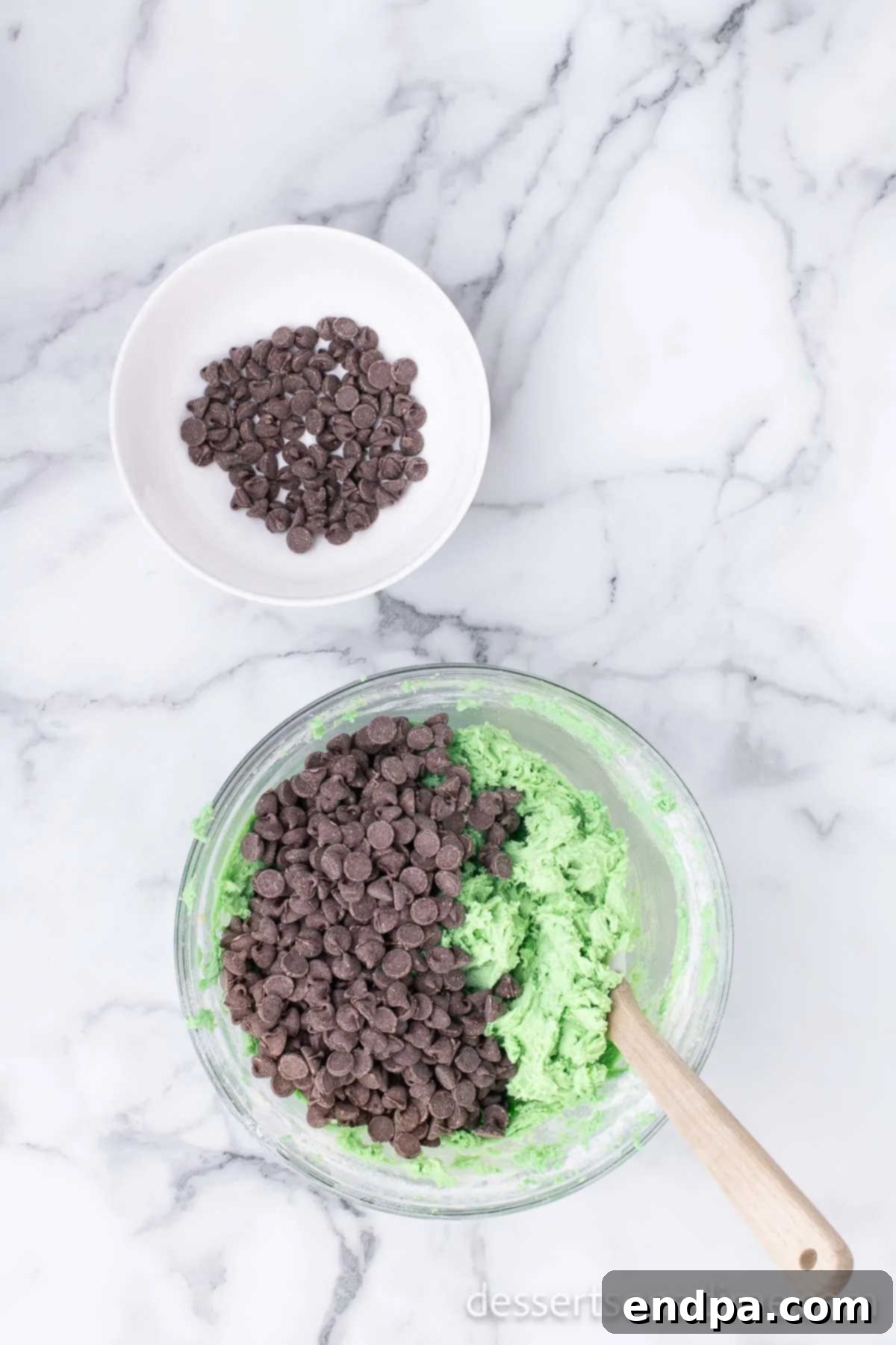 Folding semi-sweet chocolate chips into the vibrant green cookie dough by hand.