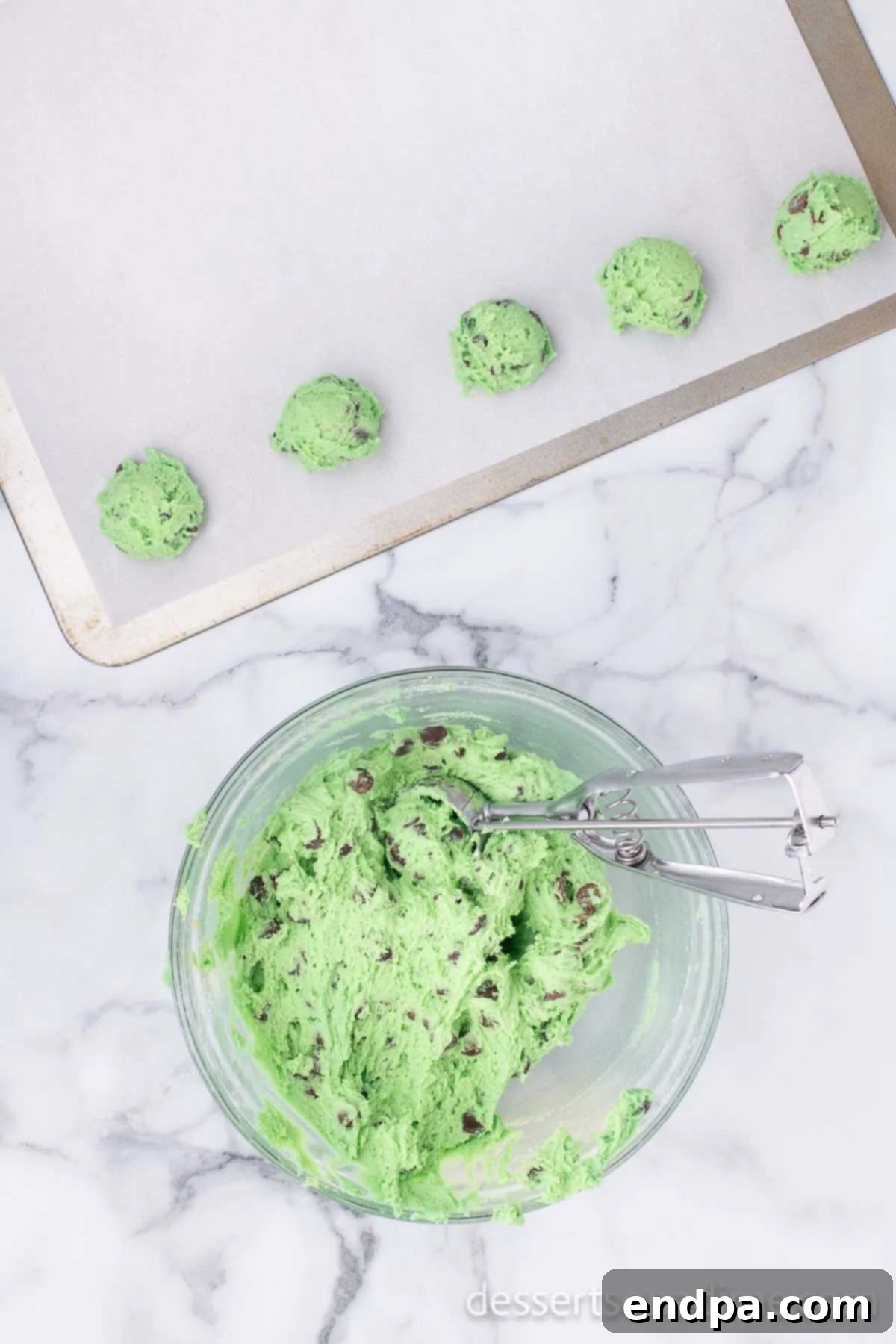 Scooping uniformed balls of mint chocolate chip cookie dough onto a baking sheet.