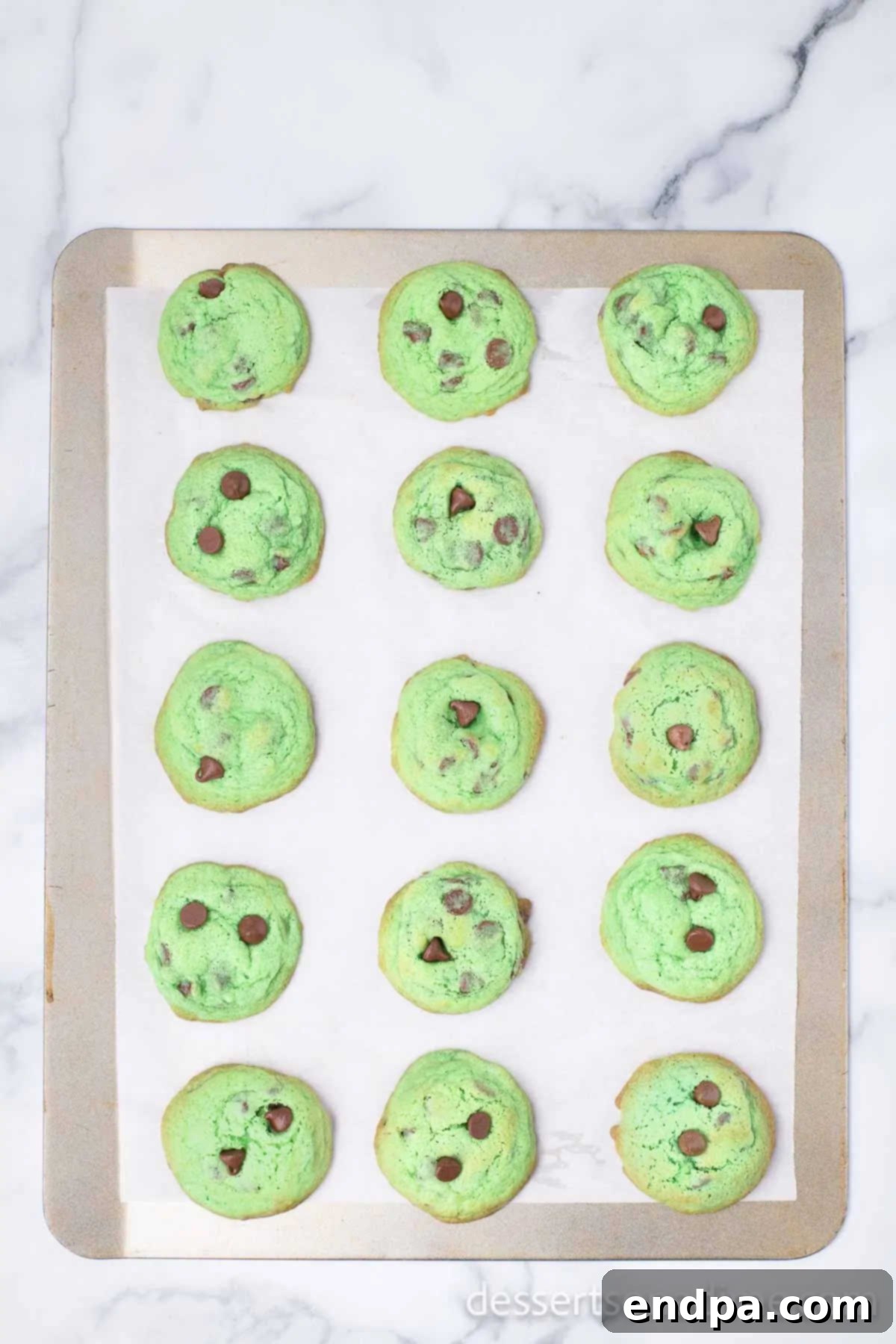 Freshly baked mint chocolate chip cookies on a baking sheet, showing slightly golden edges.