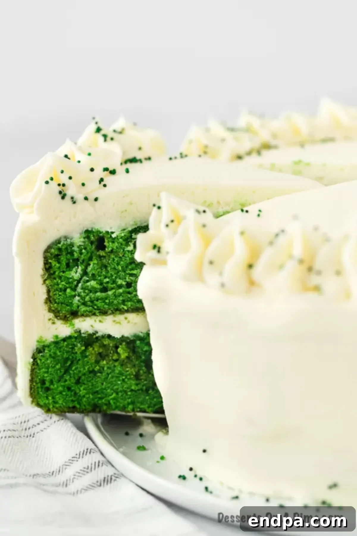 A beautifully decorated Green Velvet Cake on a stand, ready to be served, with a knife poised for slicing.