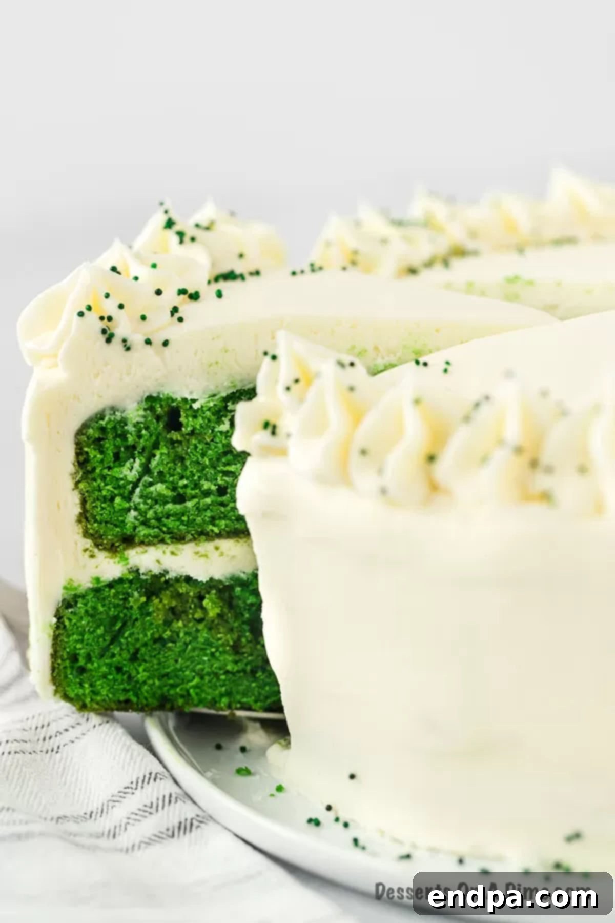 A whole Green Velvet Cake on a festive platter, decorated with cream cheese frosting and green sprinkles, ready to be enjoyed.