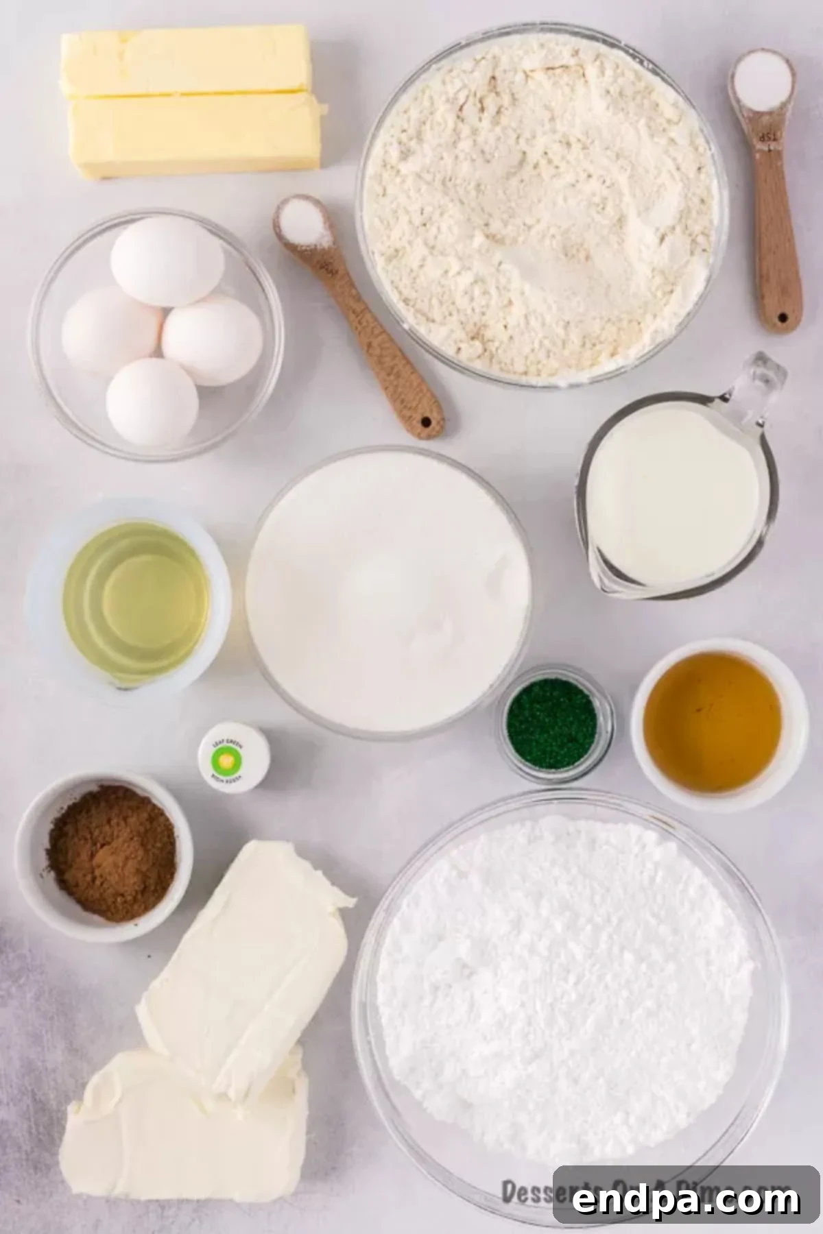 A flat lay photograph displaying all the fresh ingredients needed for Green Velvet Cake: cake flour, eggs, granulated sugar, vegetable oil, cocoa powder, vibrant green food coloring, festive green sprinkles, cream cheese, and powdered sugar.