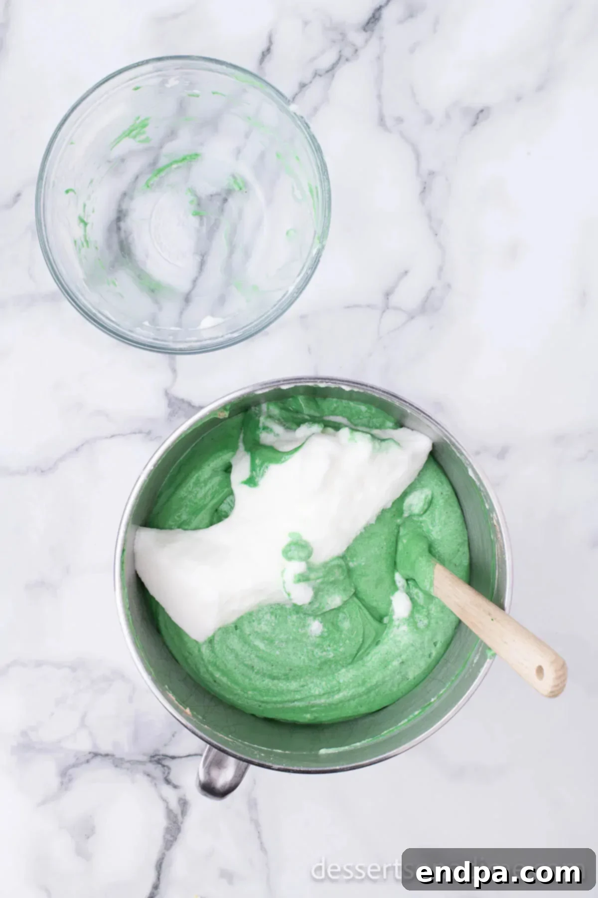 Mixing bowl with fluffy egg whites being gently folded into the green cake batter.