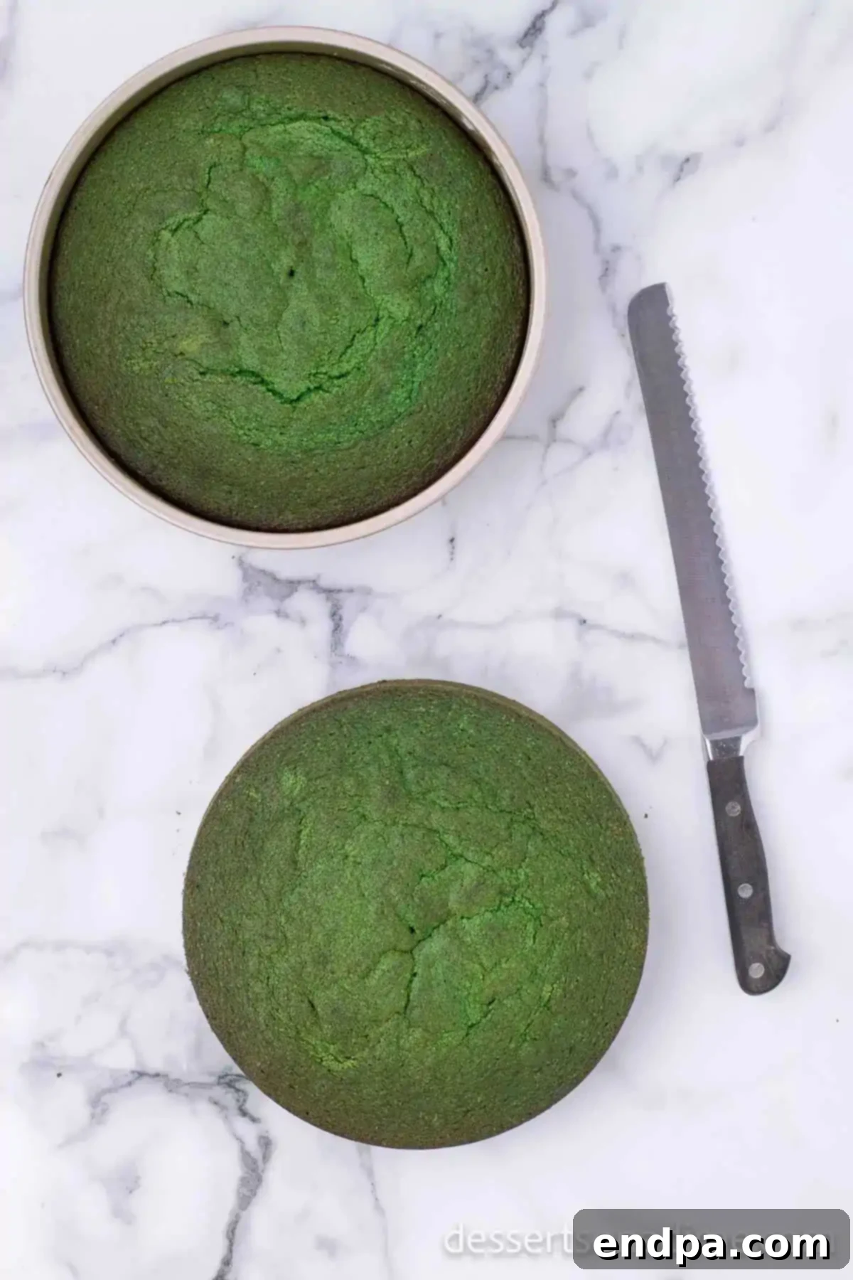 Two baked green velvet cake layers cooling in their pans on a wire rack.