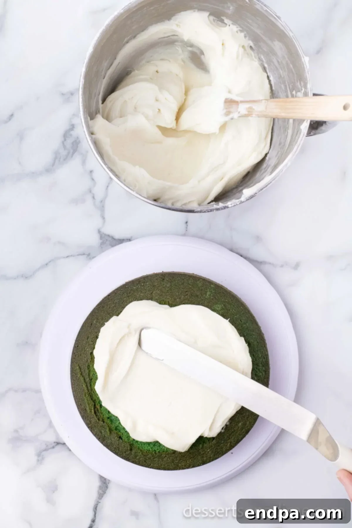 Creamy white frosting in a bowl, with a spatula spreading it evenly onto baked cake layers.