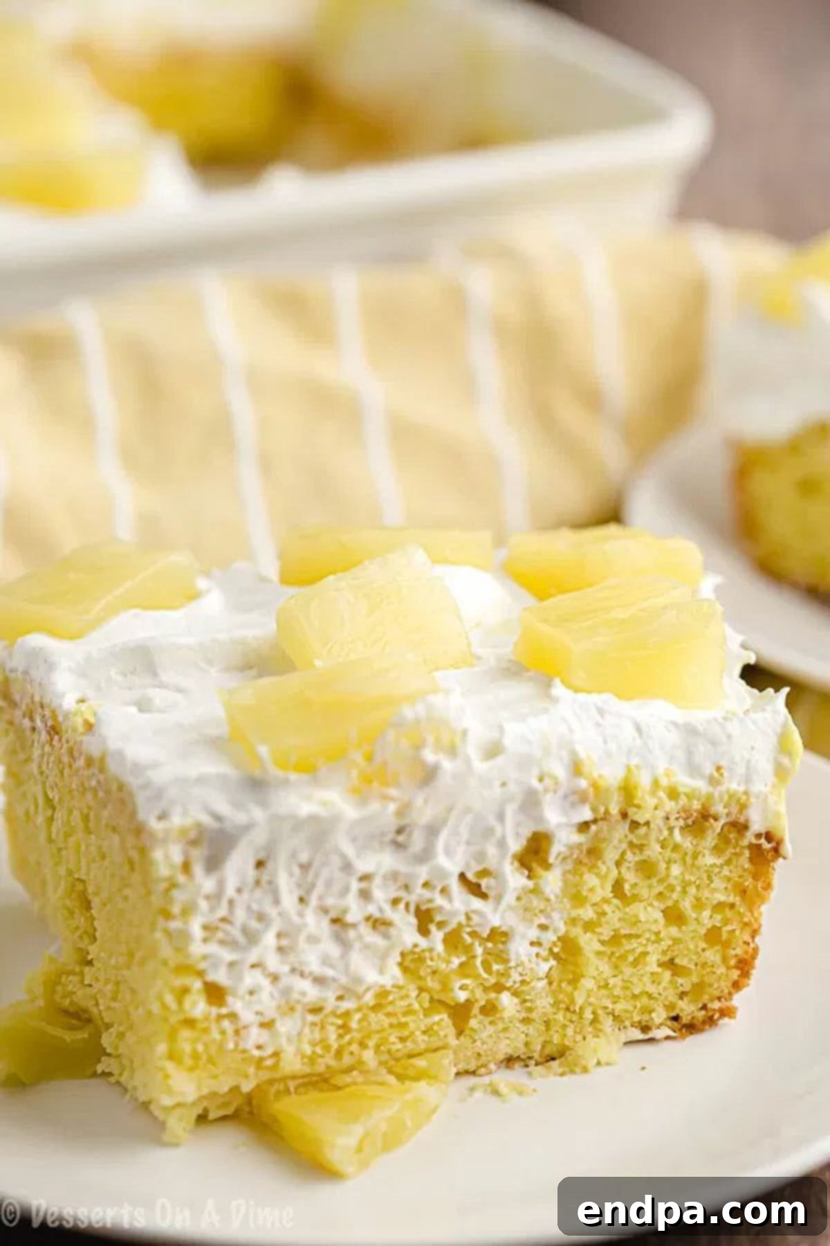 Delicious Pineapple Poke Cake Recipe: Moist, Flavorful, and Easy to Make for Any Occasion A slice of moist pineapple poke cake on a white plate, adorned with diced pineapple pieces on top.