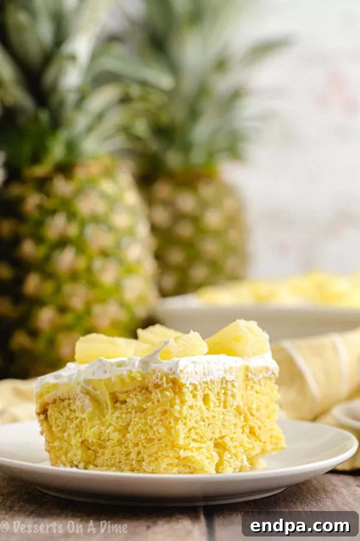 Tropical Pineapple Poke Cake 5 A serving of pineapple poke cake on a white plate, with the remaining cake in the background.
