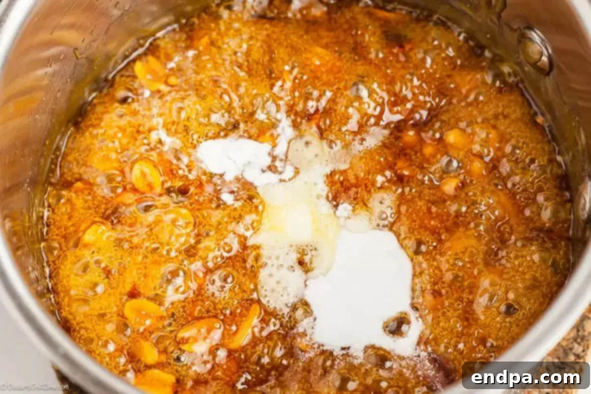 Roasted peanuts being gently stirred into the shimmering golden corn syrup and sugar mixture.