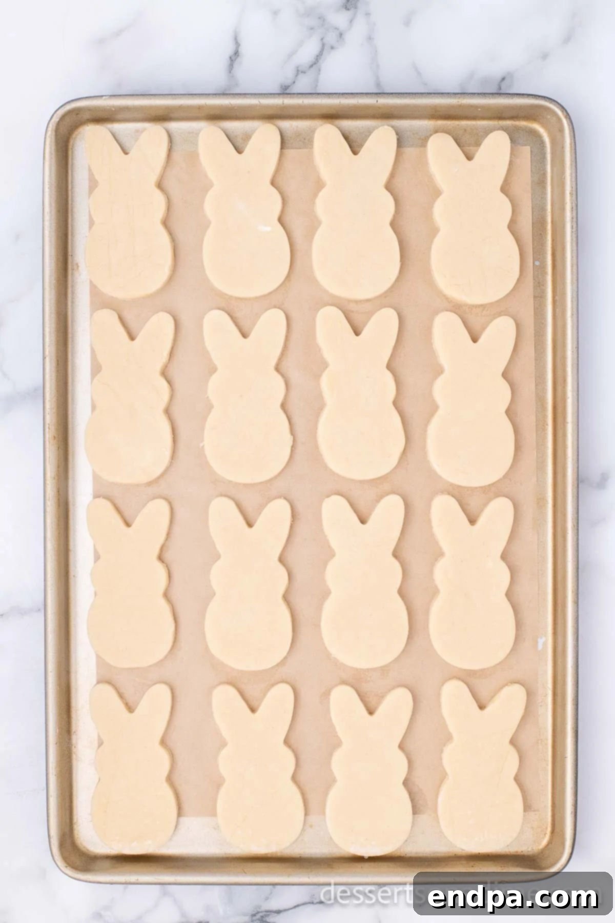 Hoppy Easter Cookie Creations 8 Bunny-shaped cookies neatly arranged on a baking sheet lined with parchment paper, ready for the oven.