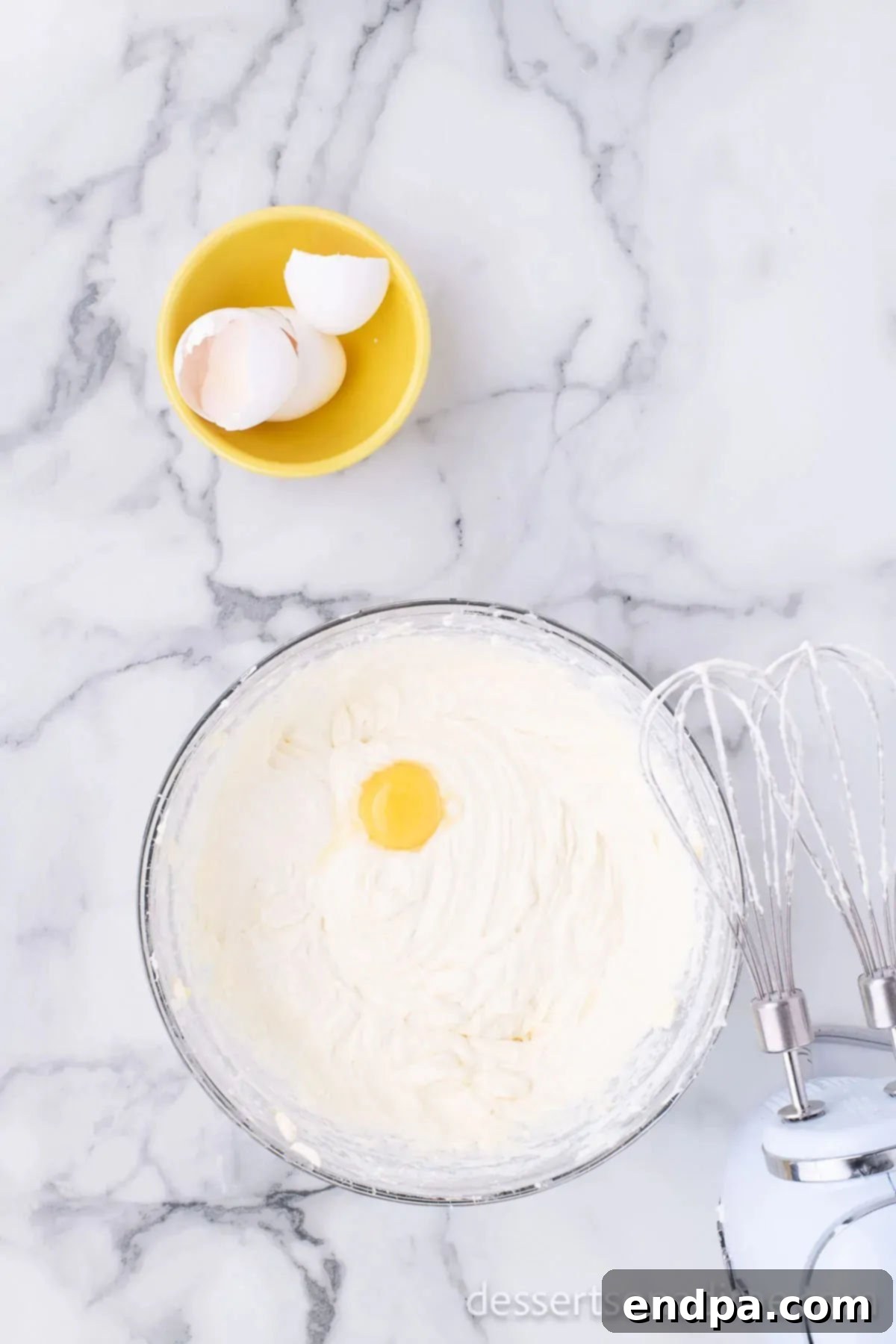 Decadent Strawberry Shortcake Cheesecake 7 Eggs being added one by one to the cream cheese mixture in a mixing bowl.