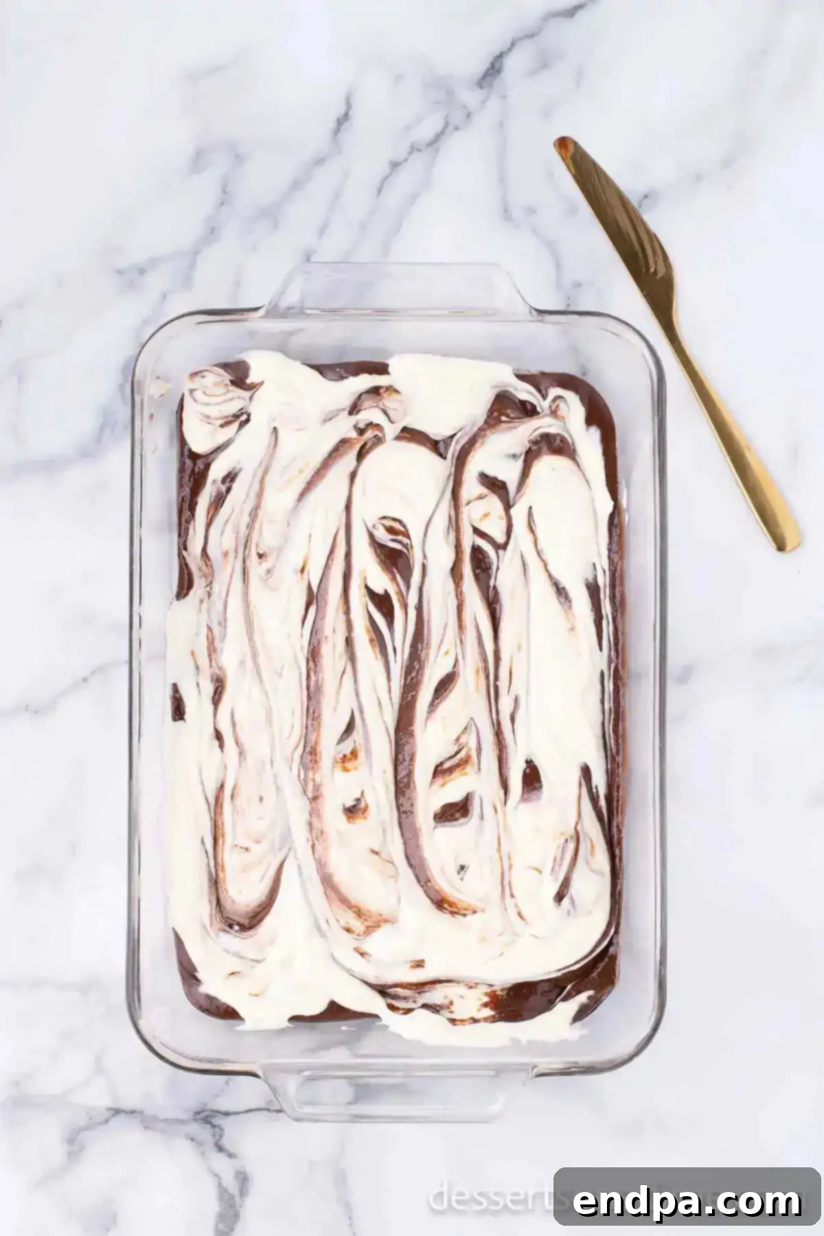 Creamy cheesecake mixture swirled elegantly on top of the raw brownie batter in a baking pan.
