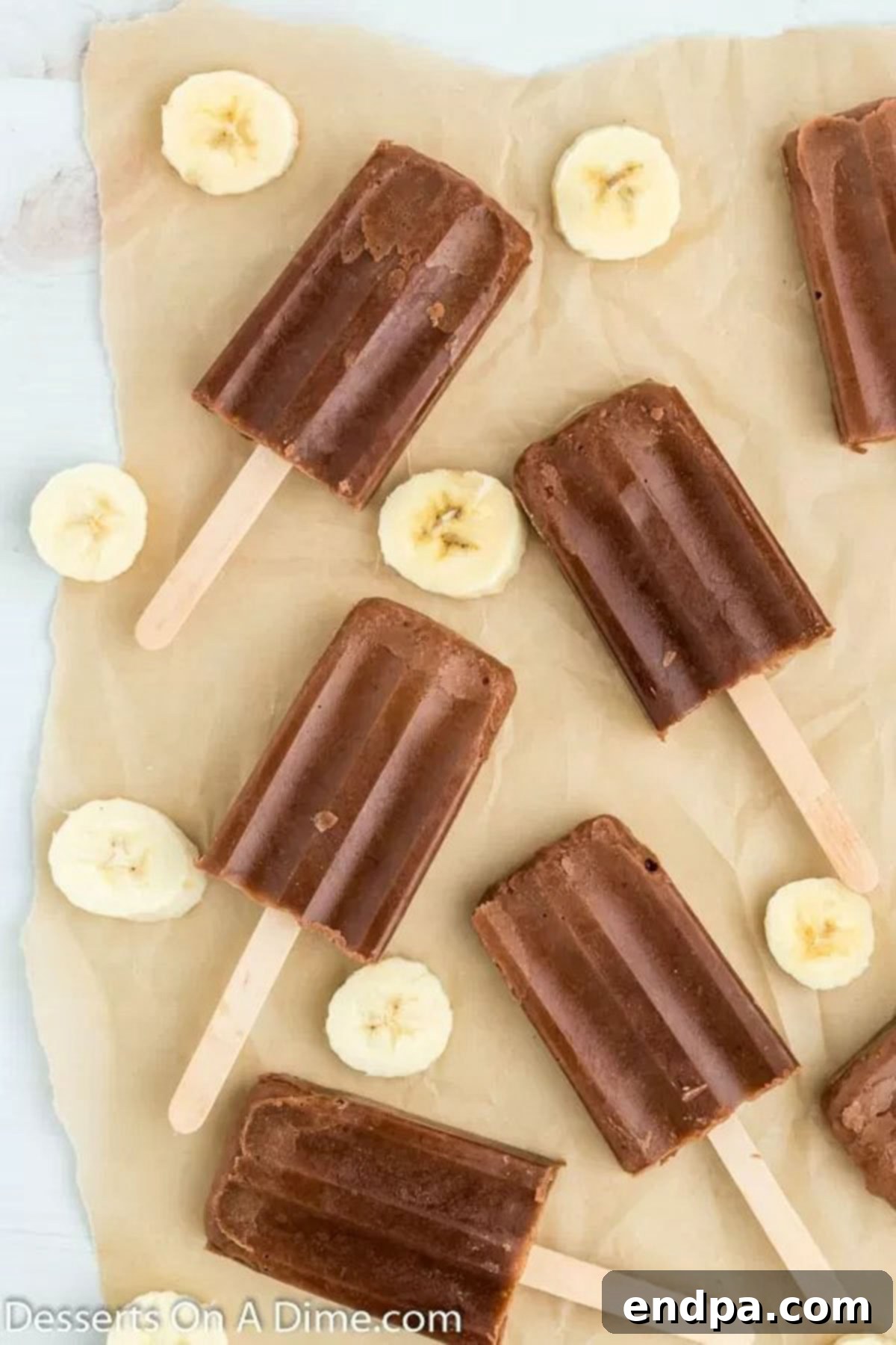 Creamy homemade chocolate banana popsicles on wax paper, ready to be enjoyed.