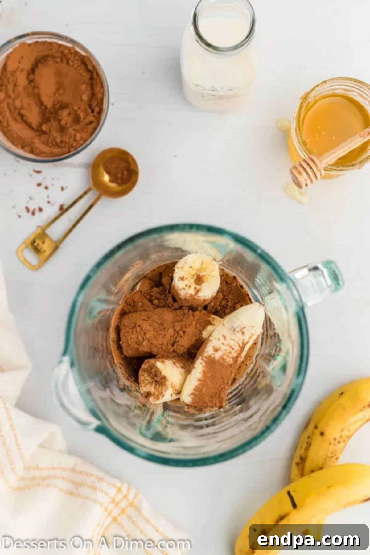 Almond milk, bananas, cocoa powder, and honey are added to a blender for the popsicle mixture.