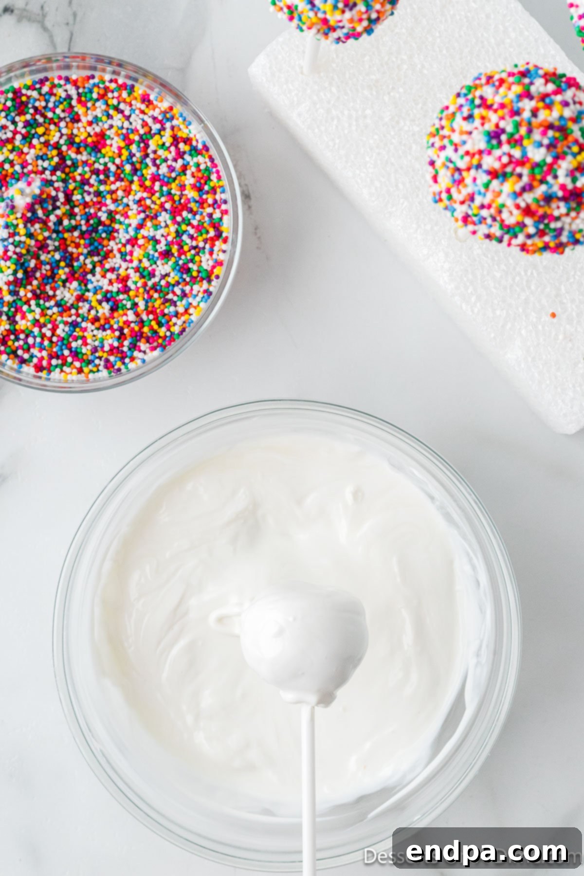 Cake balls dipped smoothly in melted white candy coating, dripping excess.