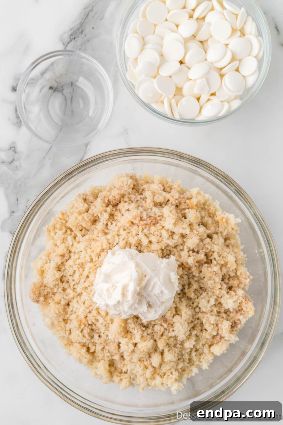 White frosting being added to the crumbled cake in a bowl.