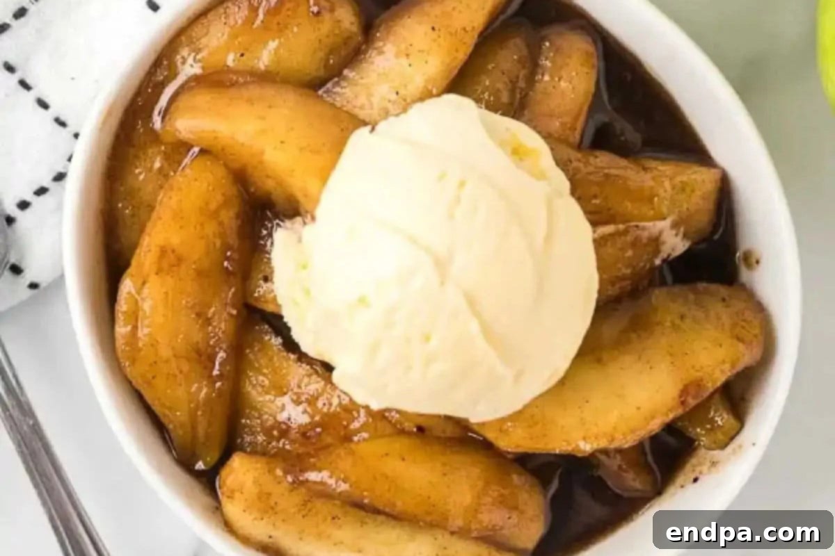 Fried apples in a bowl topped with ice cream and a spoon, ready to be eaten.