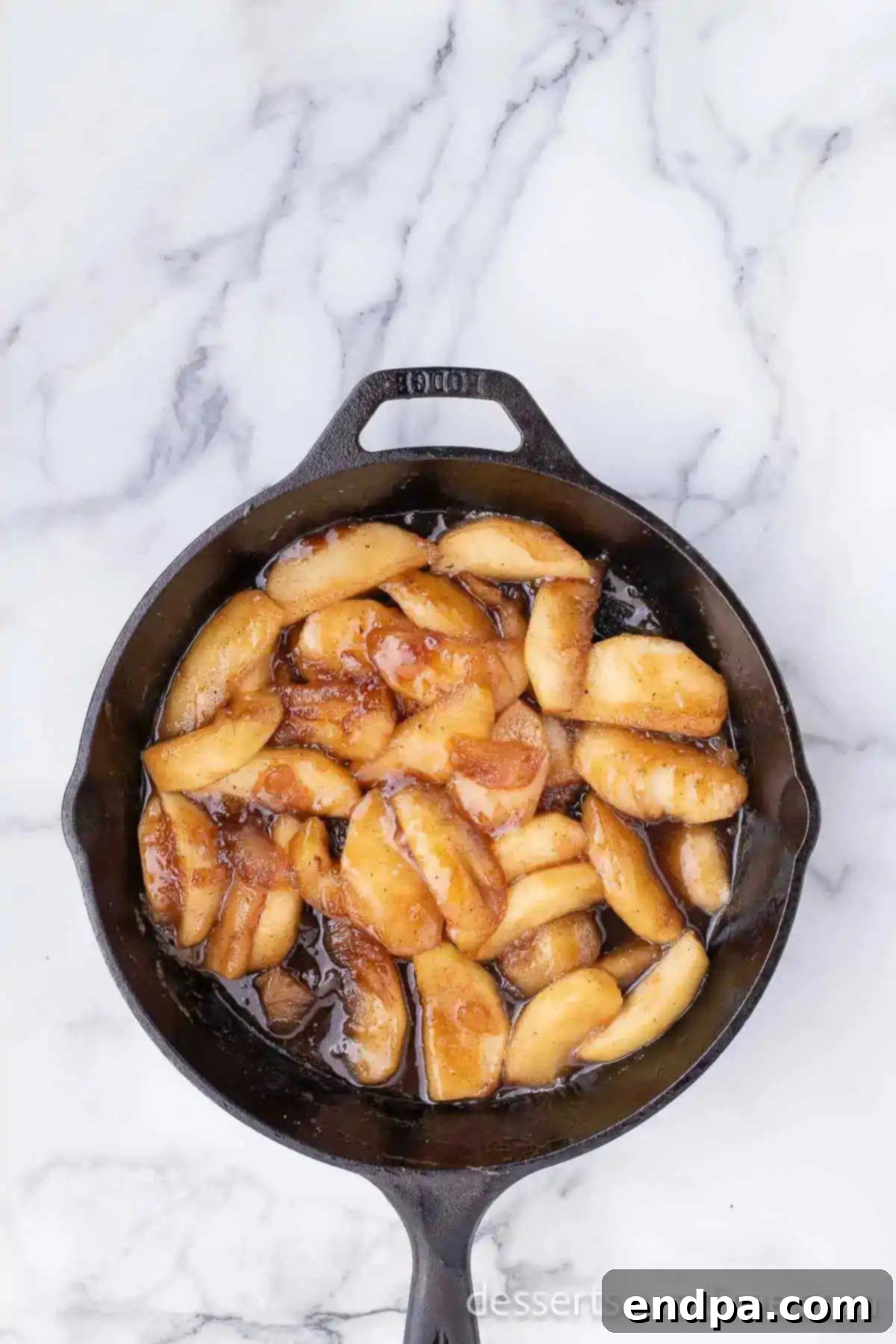 Apple slices being stirred in a skillet with the butter, cinnamon, and sugar mixture.