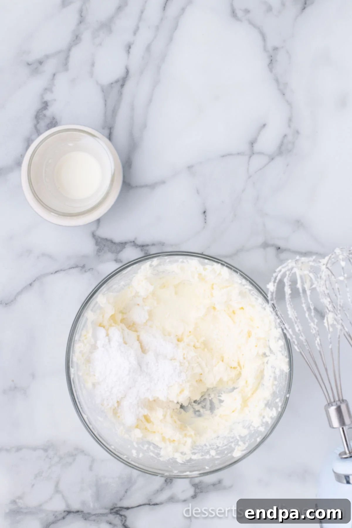 A bowl of smooth, pale cream cheese mixture, whipped to a light consistency with an electric mixer.
