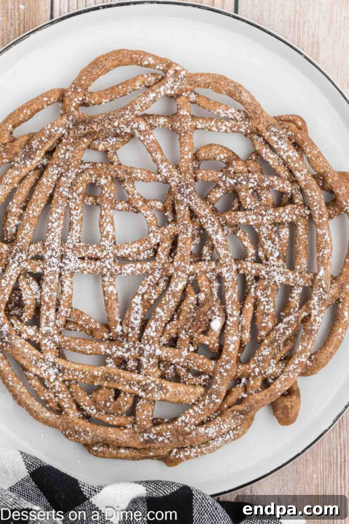 A beautifully fried chocolate funnel cake on a white plate, generously dusted with powdered sugar, ready to be enjoyed.